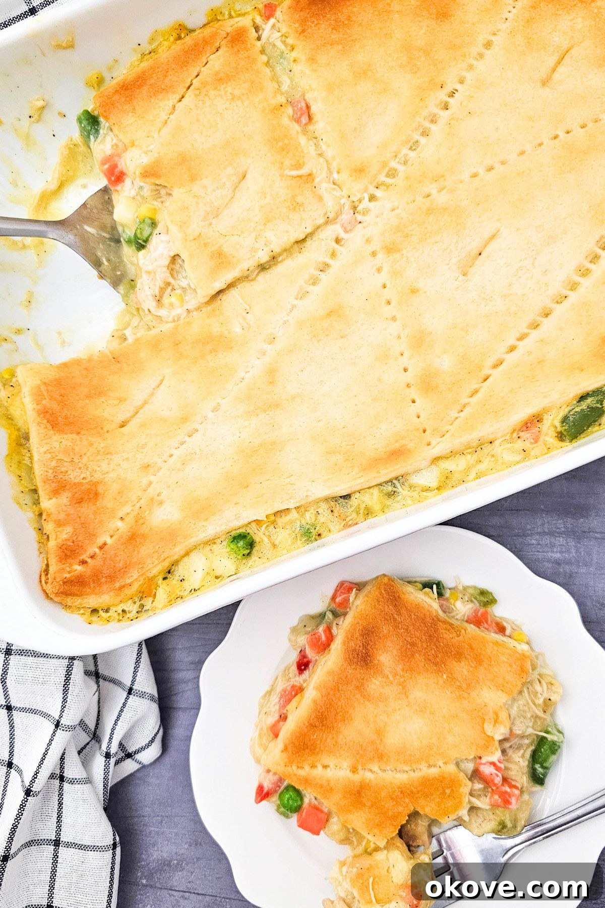Homestyle Chicken Pot Pie Bake 9 A golden-crusted chicken pot pie casserole in a baking dish with one slice removed and placed on a white plate, showcasing the creamy filling.