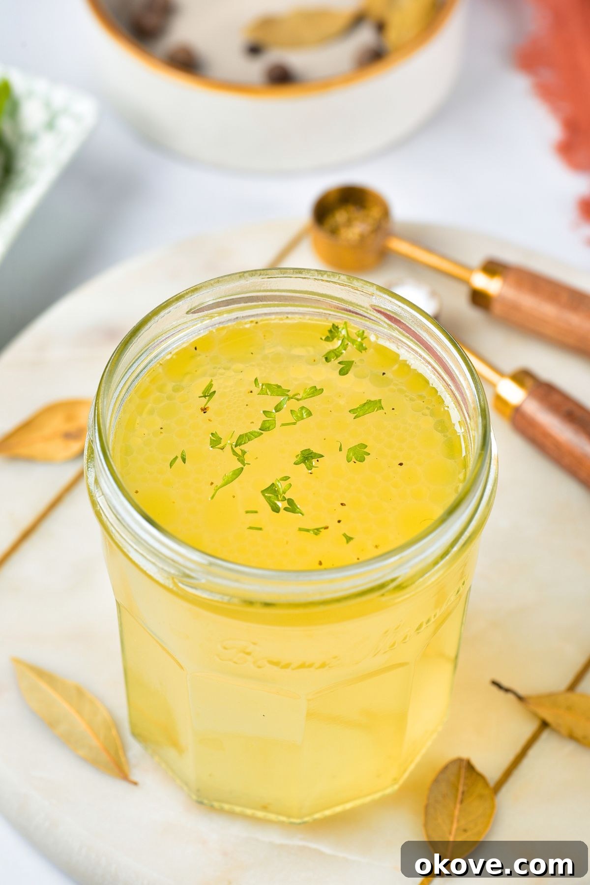 Small jar filled with golden yellow homemade chicken stock, signifying richness and quality.
