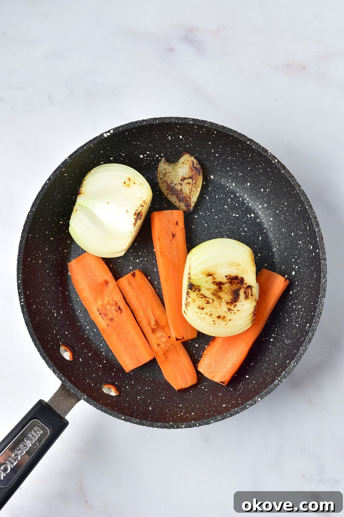 Halved carrots and onions being slightly charred in a dry skillet over medium-high heat.