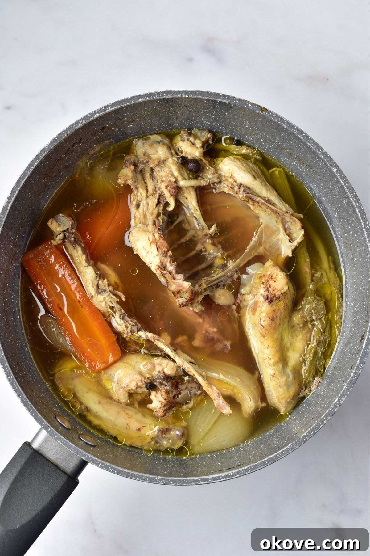 A stockpot simmering gently with chicken, vegetables, and herbs, showing a rich, clear liquid.