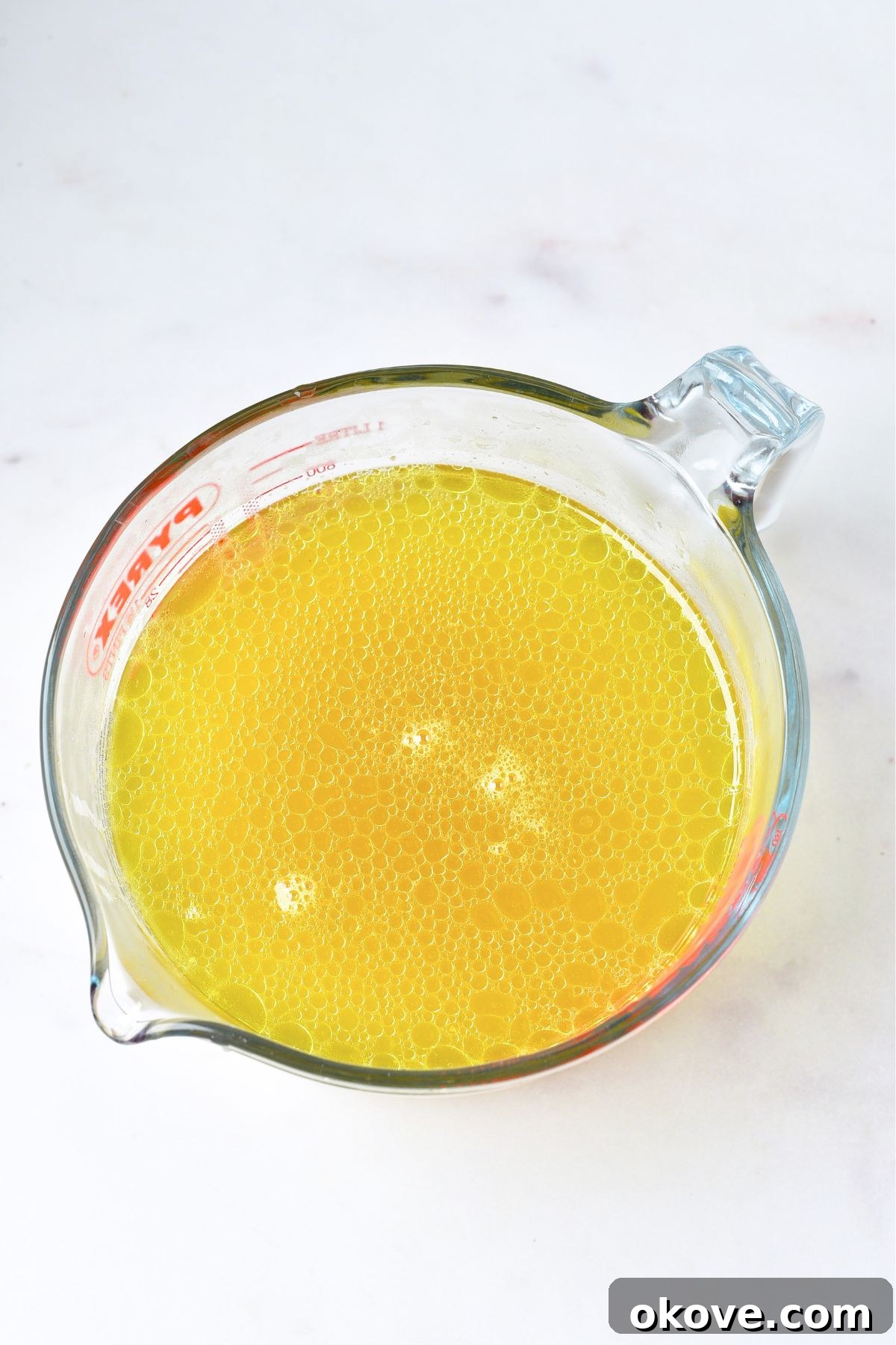 A measuring cup filled with strained homemade chicken stock, showing its golden color and clarity.