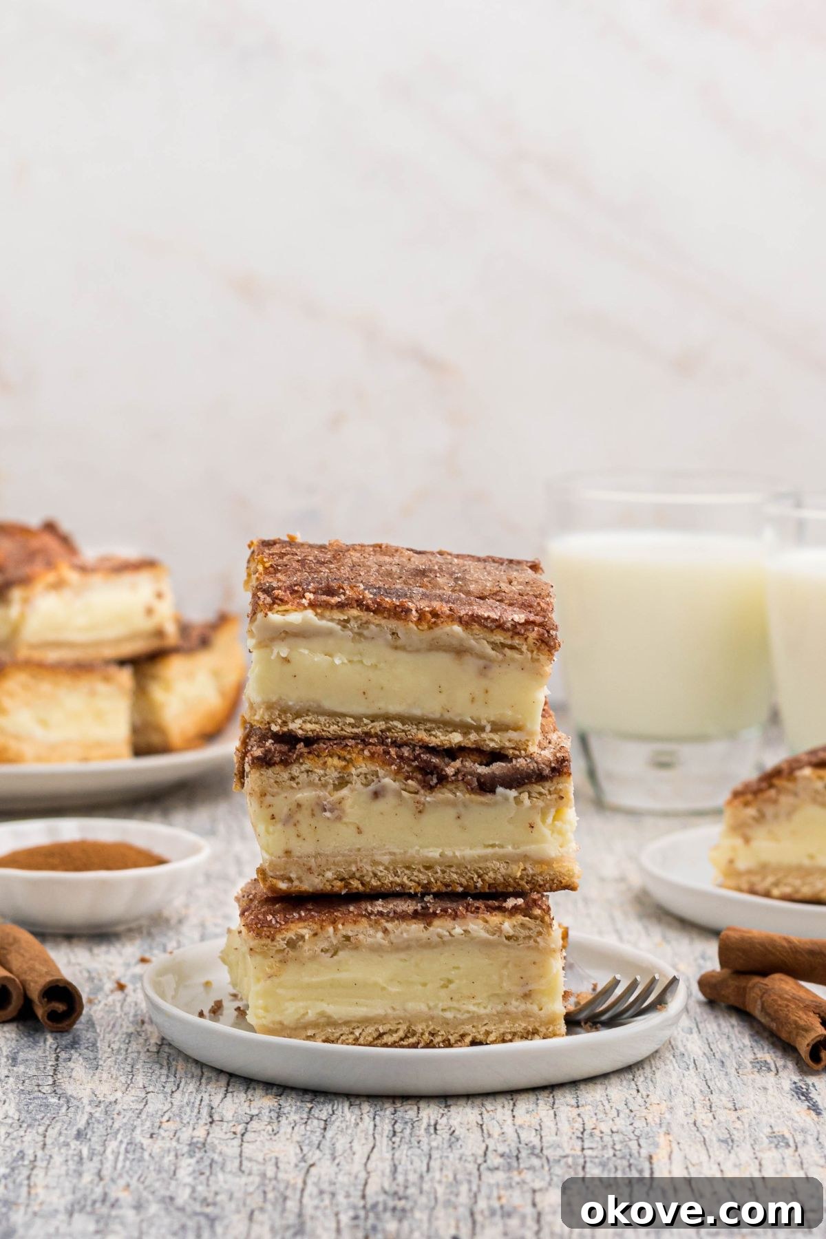 Cinnamon Sugar Crust Cheesecake 11 Three slices of churro cheesecake, stacked on a small white plate in front of glasses of milk.