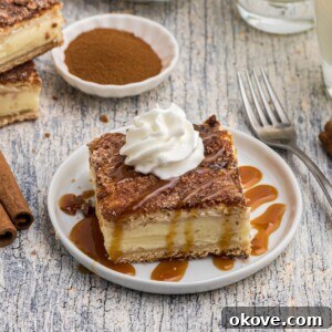 Slice of churro cheesecake served on a small white plate in front of glasses of milk, with a drizzle of caramel sauce and whipped cream on top.