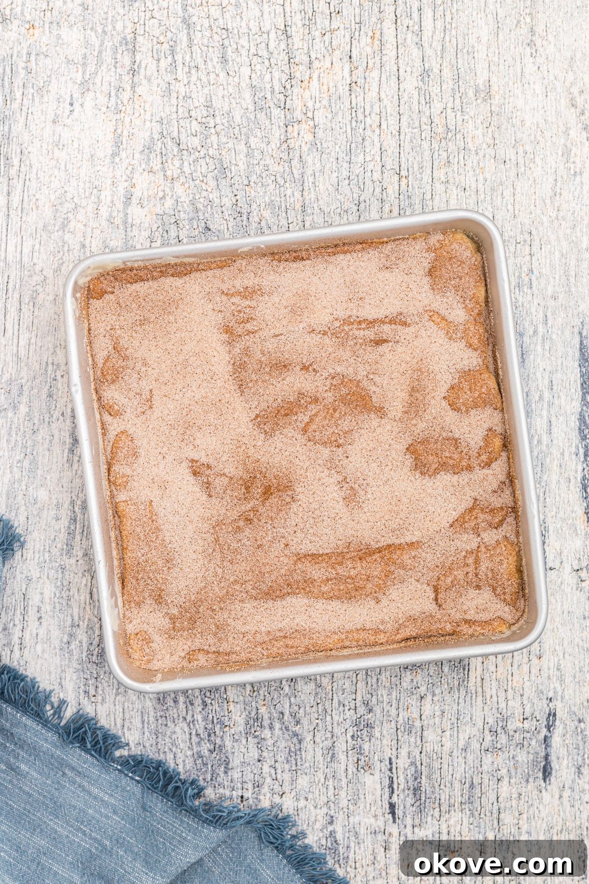 Cinnamon Sugar Crust Cheesecake 9 Top of square cheesecake topped with melted butter and sugar and cinnamon mixture, before baking.