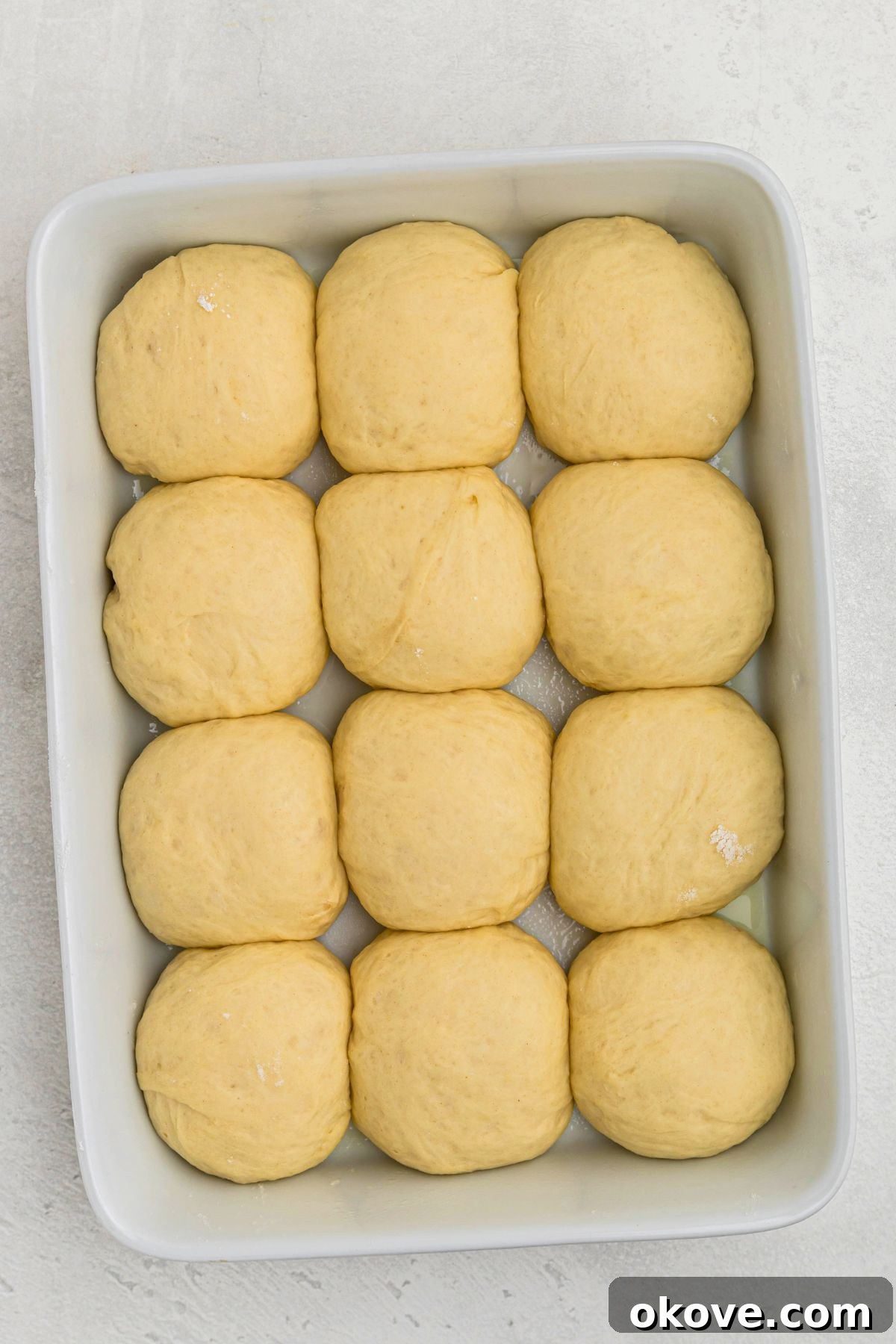 Warm Golden Dinner Rolls 11 Uncooked dinner rolls, visibly risen a second time, filling the white baking dish and looking puffy and ready to be transferred to the oven for baking.
