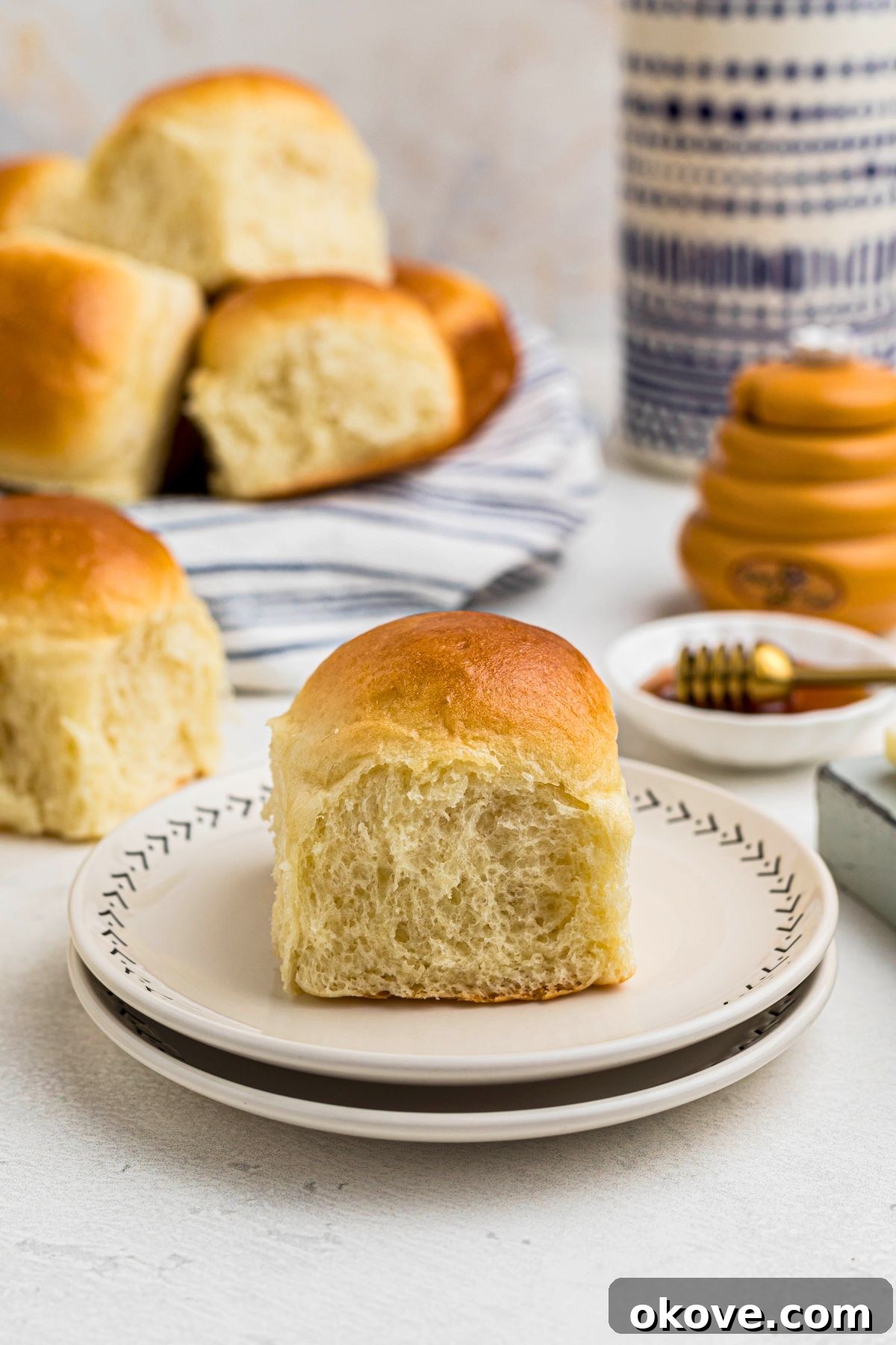 Warm Golden Dinner Rolls 12 A single golden-baked dinner roll presented elegantly on a small white plate, showing its soft, fluffy interior, ready to be enjoyed.