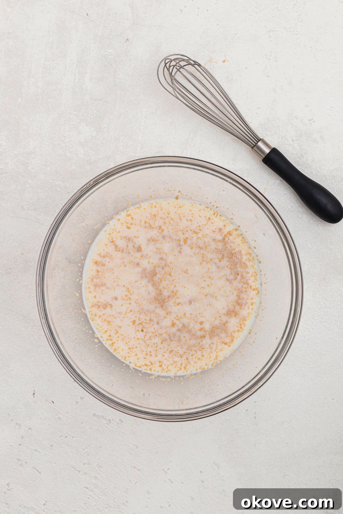 Warm Golden Dinner Rolls 4 Active dry yeast, warm milk, and granulated sugar combined in a clear glass bowl, beginning to activate and show initial signs of foam.