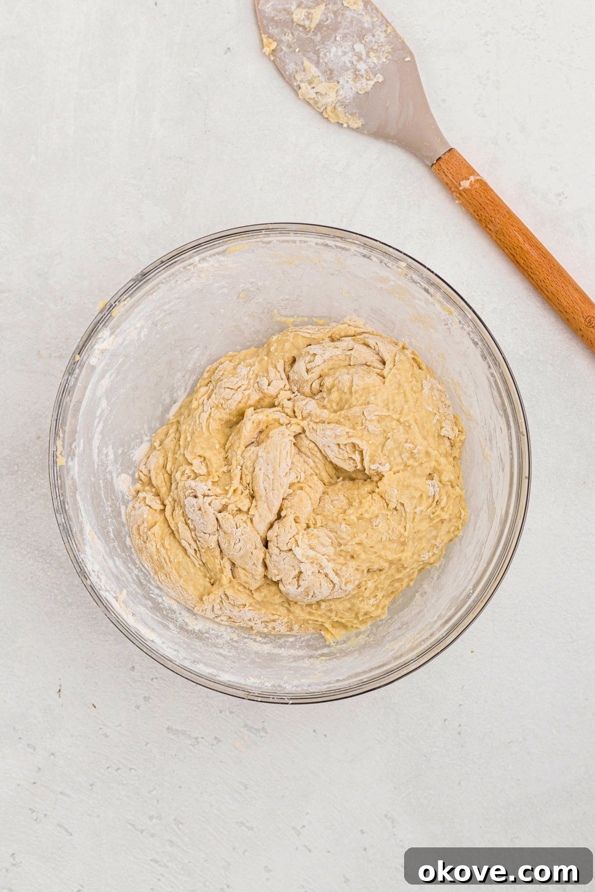 Warm Golden Dinner Rolls 6 Bread dough ingredients being thoroughly mixed together in a large clear glass bowl to form a cohesive, shaggy dough before kneading.