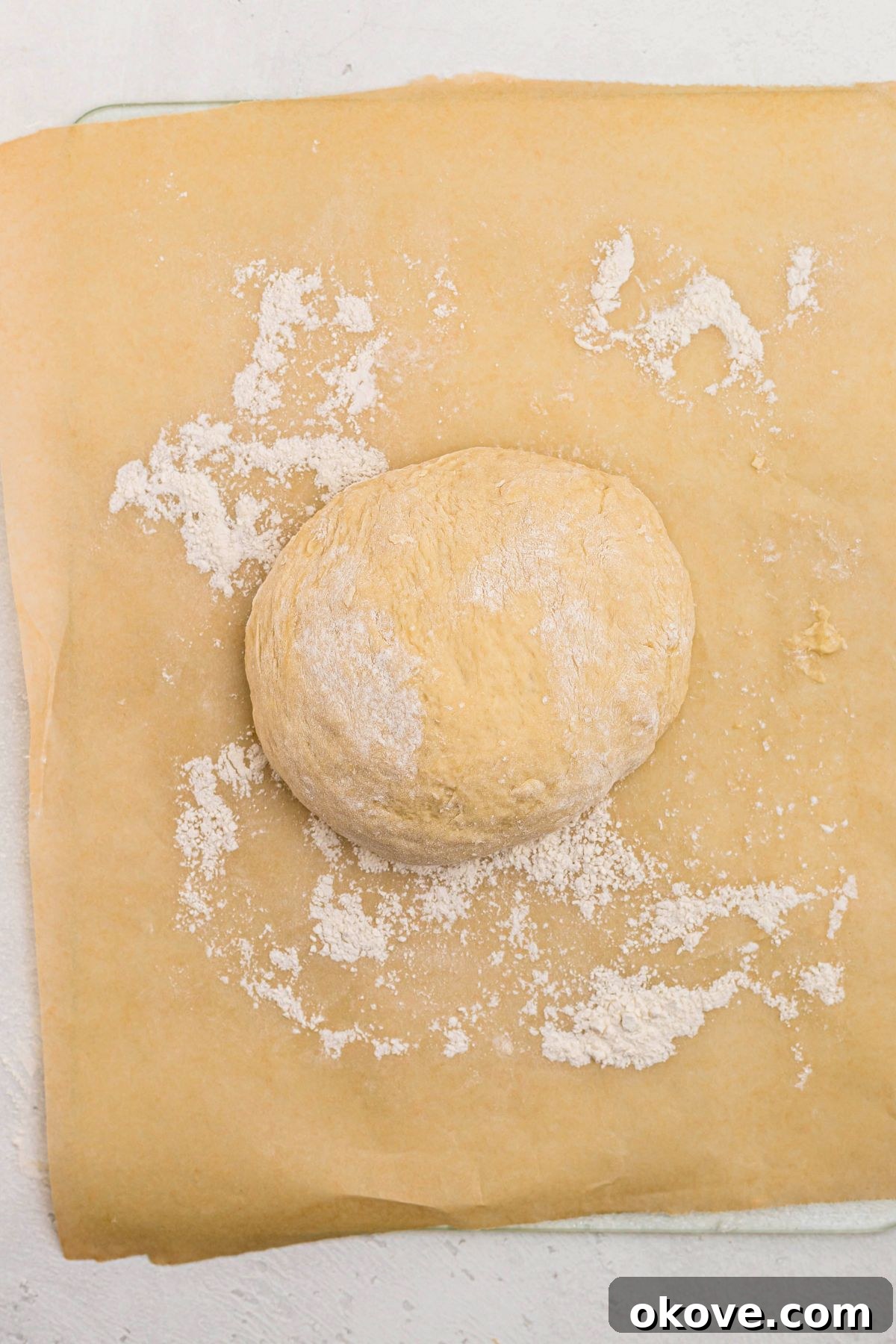 Warm Golden Dinner Rolls 7 A smooth, elastic ball of bread dough resting on a lightly floured surface, perfectly kneaded and ready for its first rise.