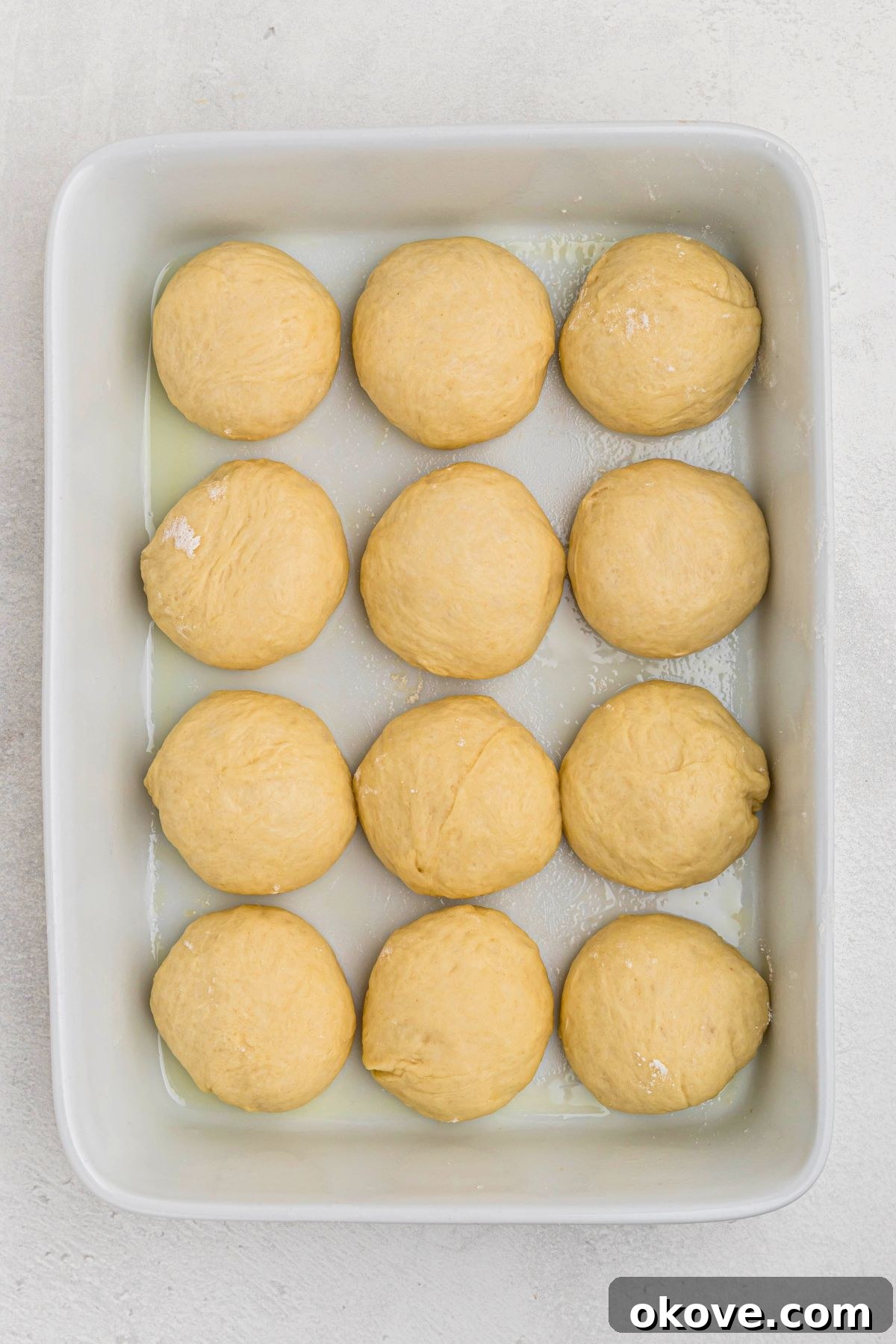 Warm Golden Dinner Rolls 10 Neatly shaped, uncooked roll dough balls arranged in a greased white 9x13 inch baking dish, with small gaps, ready for their second rise.