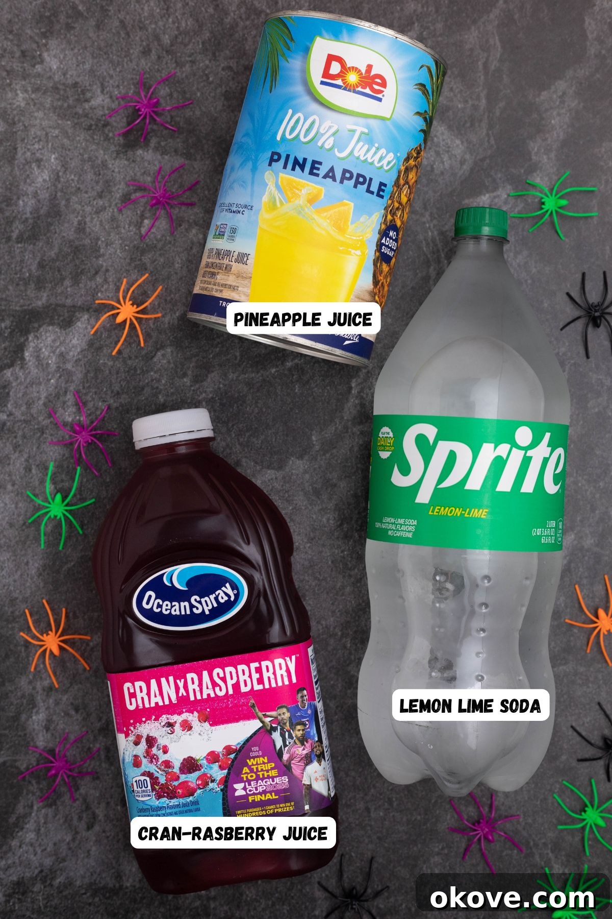 Bottles of pineapple juice, cran-raspberry juice, and lemon-lime soda on a black marble table, ready for making Halloween punch.