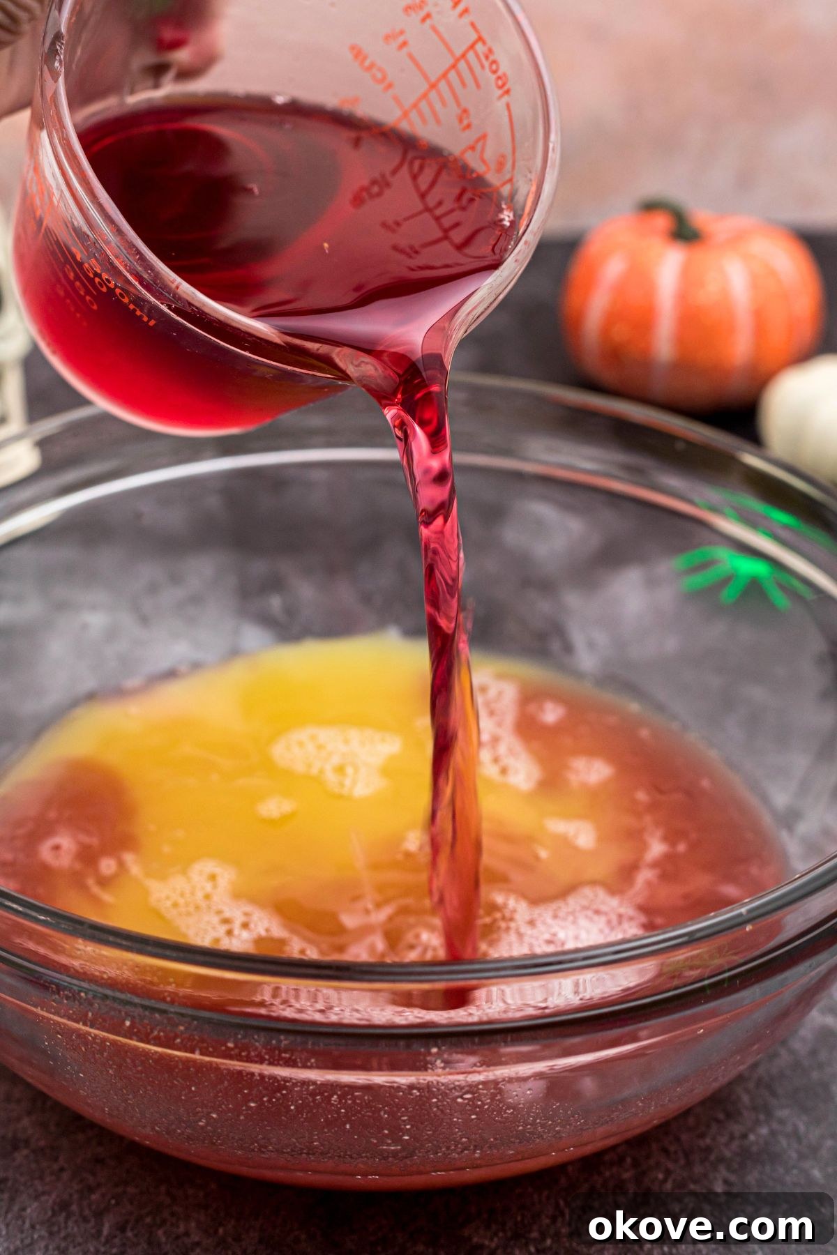 Cranberry, pineapple, and lemon-lime juices being combined in a large clear glass punch bowl, ready to be stirred.
