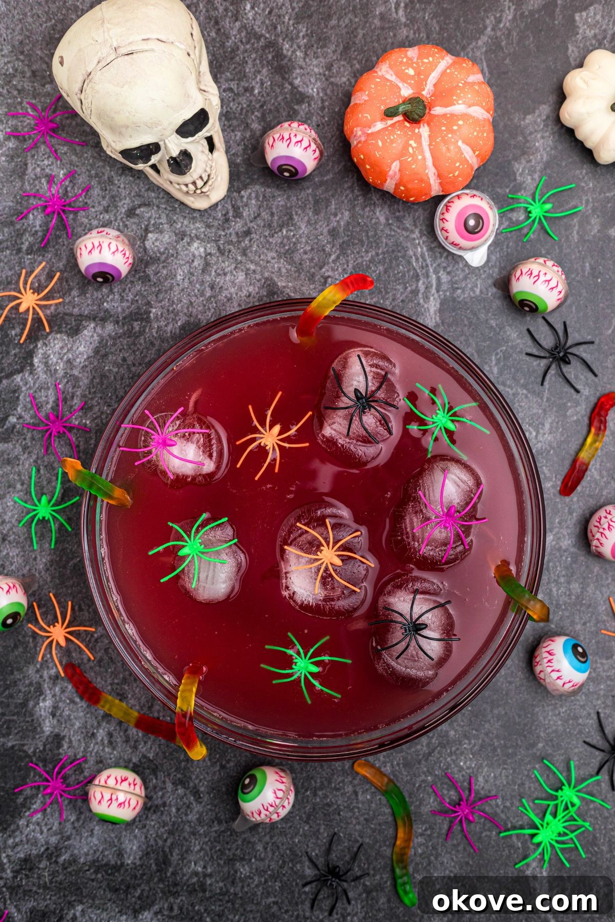 Punch bowl filled with vibrant Halloween punch, adorned with pumpkin-shaped ice cubes and plastic spiders for a festive touch.