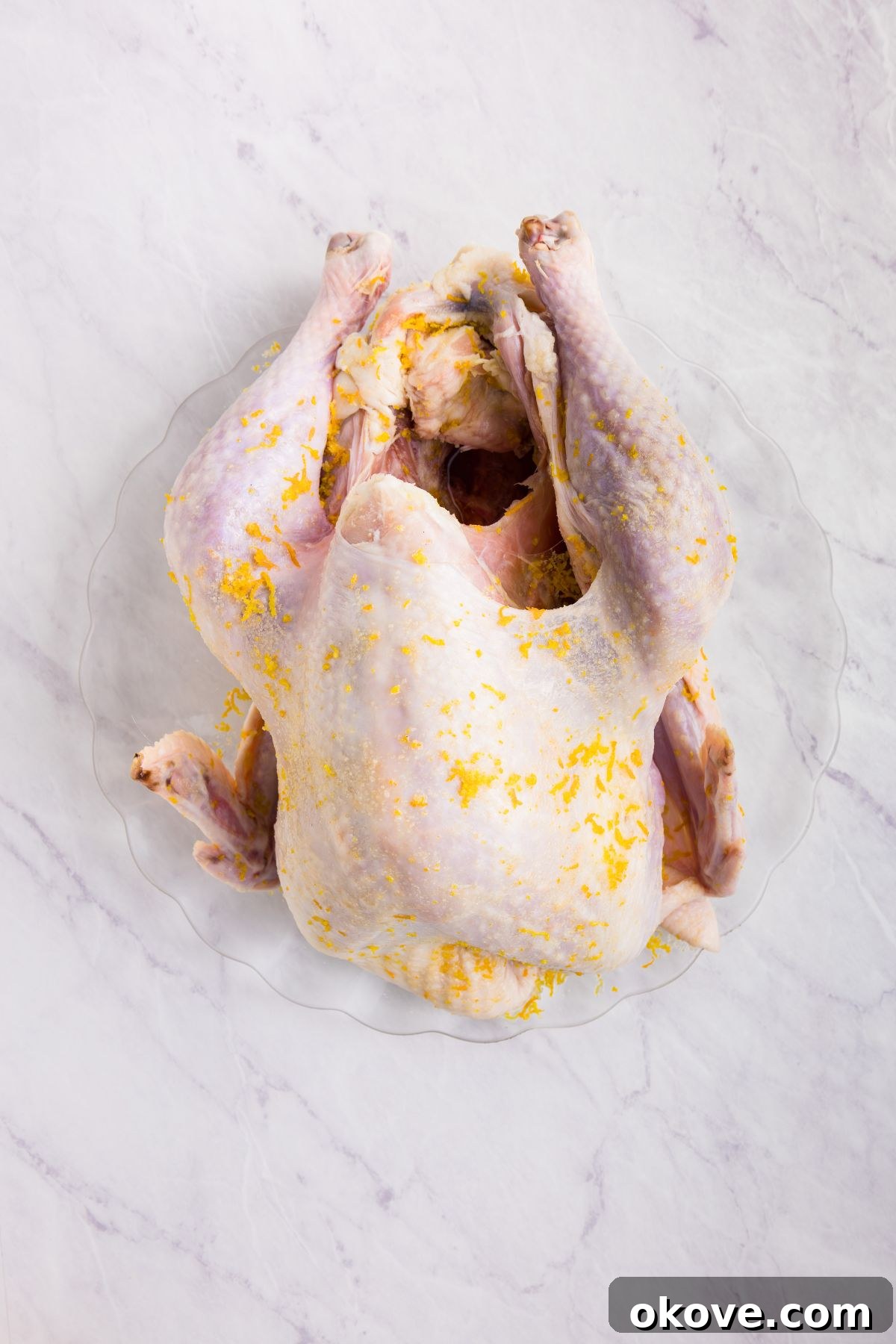 Golden Roasted Turkey Perfection 5 Uncooked chicken rubbed in a brine of seasonings and orange zest, on a marble table.