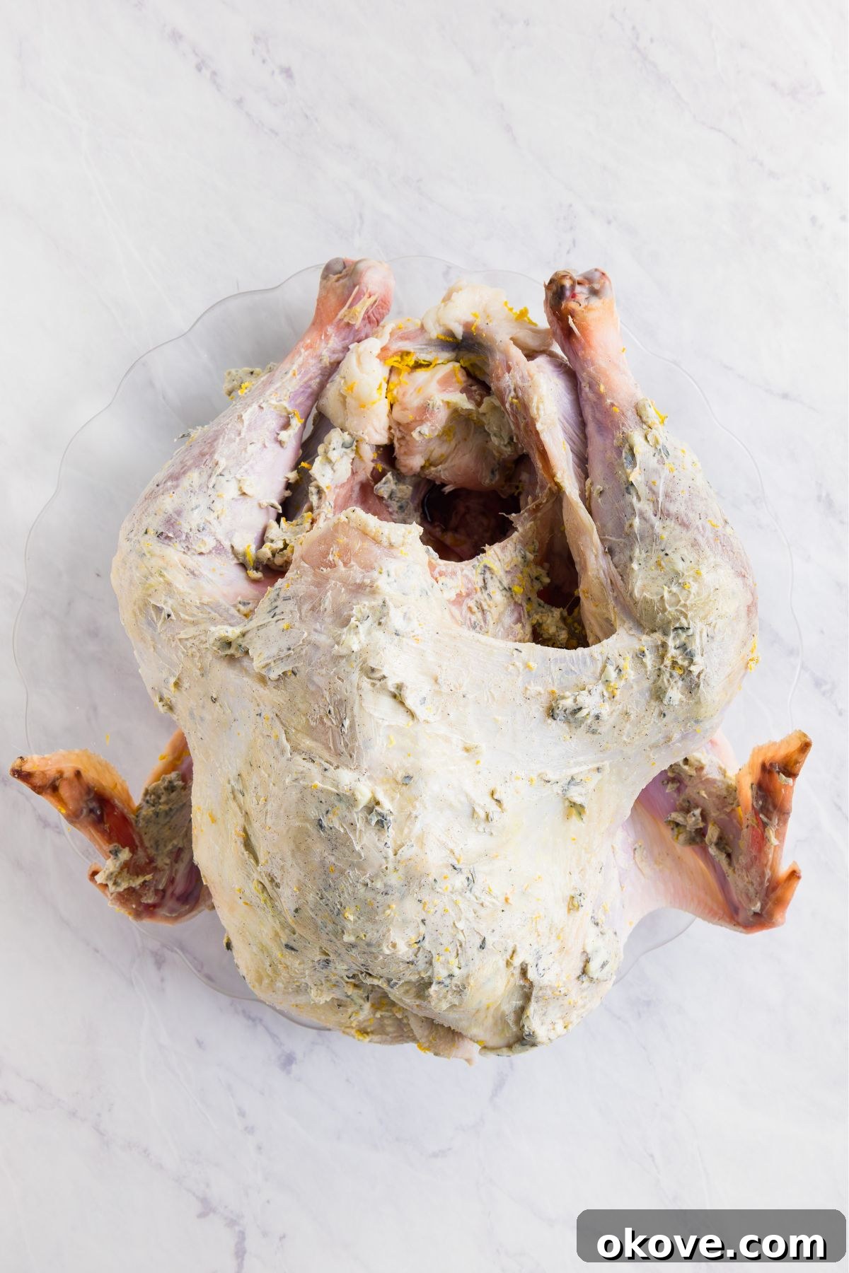 Golden Roasted Turkey Perfection 6 Uncooked turkey on a marble table, covered with a garlic herb butter.