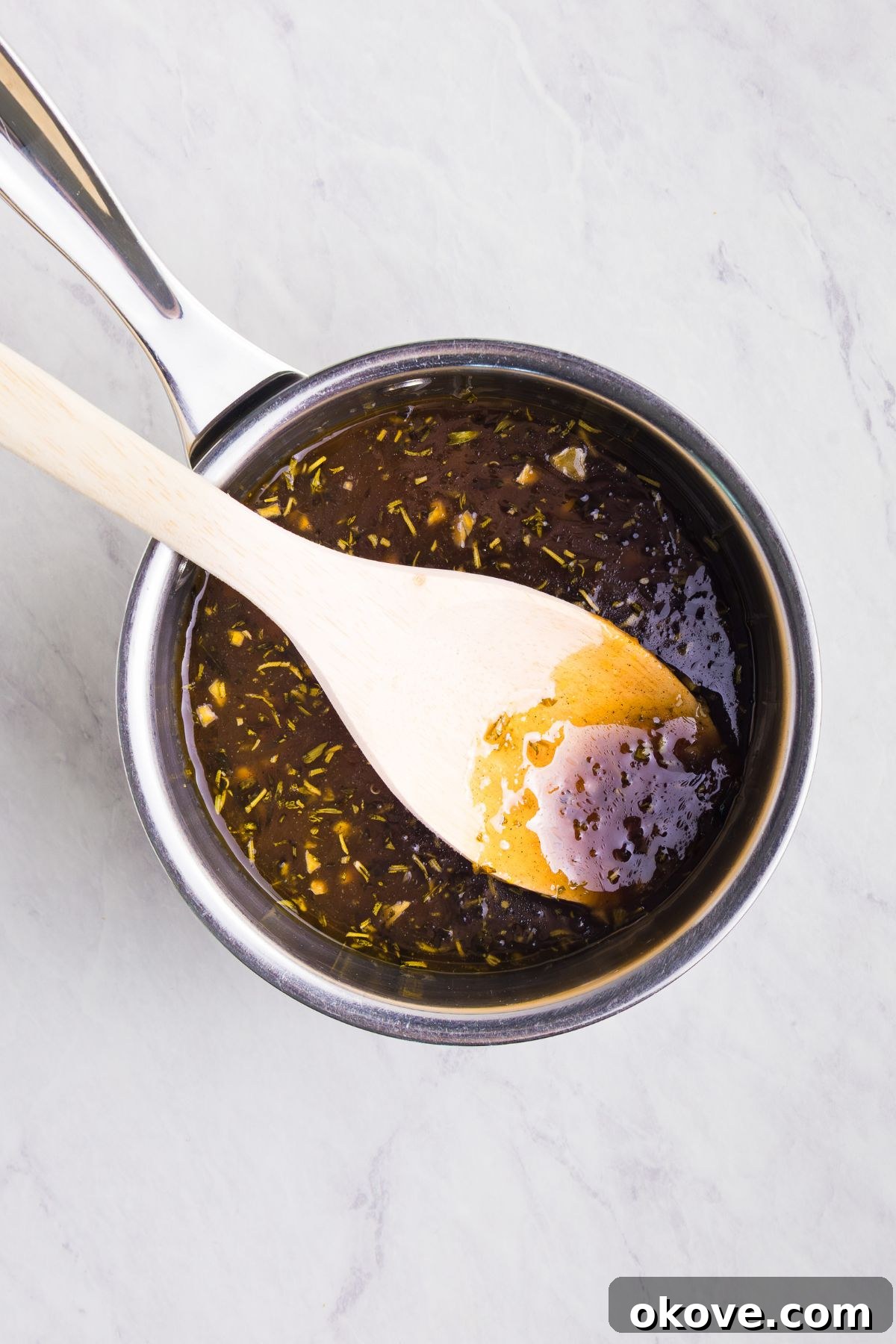 Golden Roasted Turkey Perfection 9 Saucepan with orange glaze being stirred with a white spoon, on a marble table.