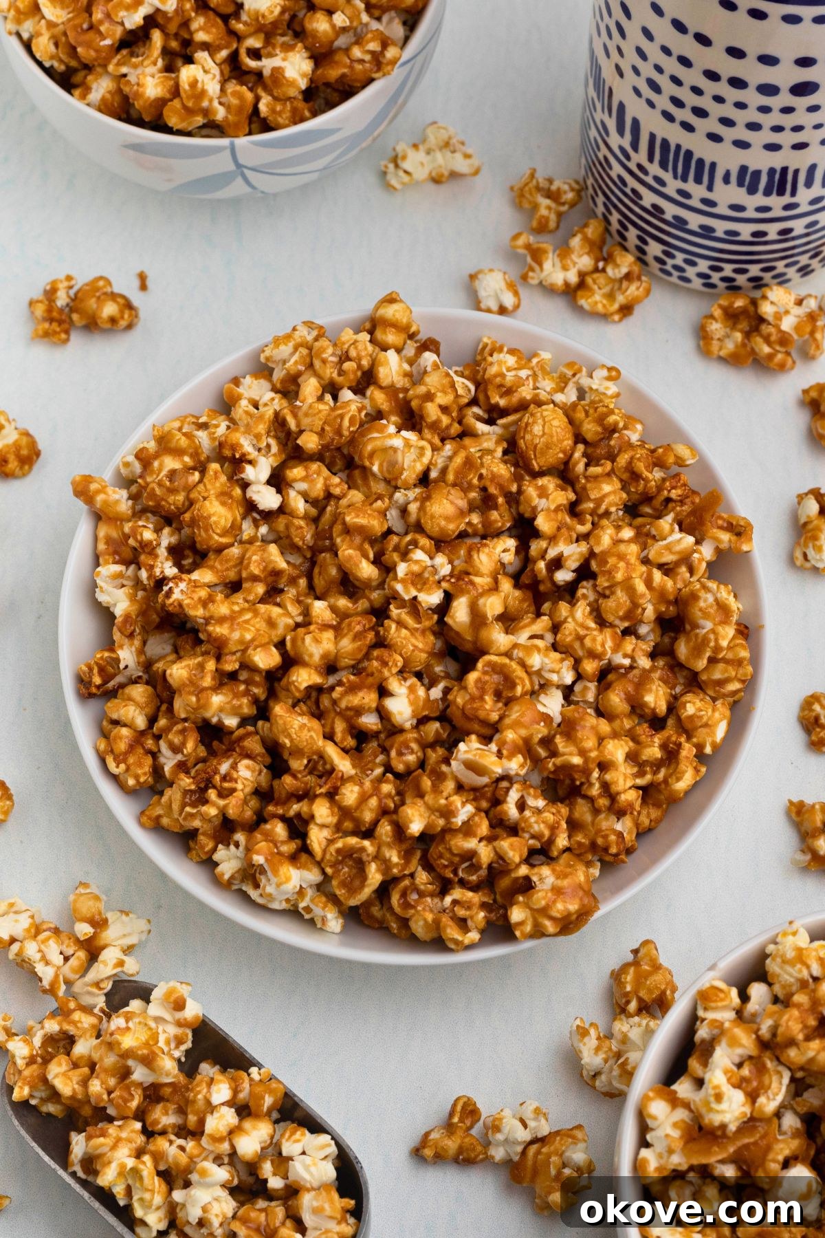 Golden Caramel Crunch 2 Golden caramel popcorn in a white bowl with pieces of popcorn scattered around the bowl.