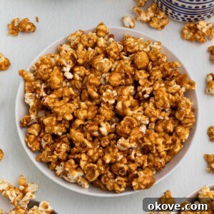Golden caramel popcorn in a white bowl with pieces of popcorn scattered around the bowl.