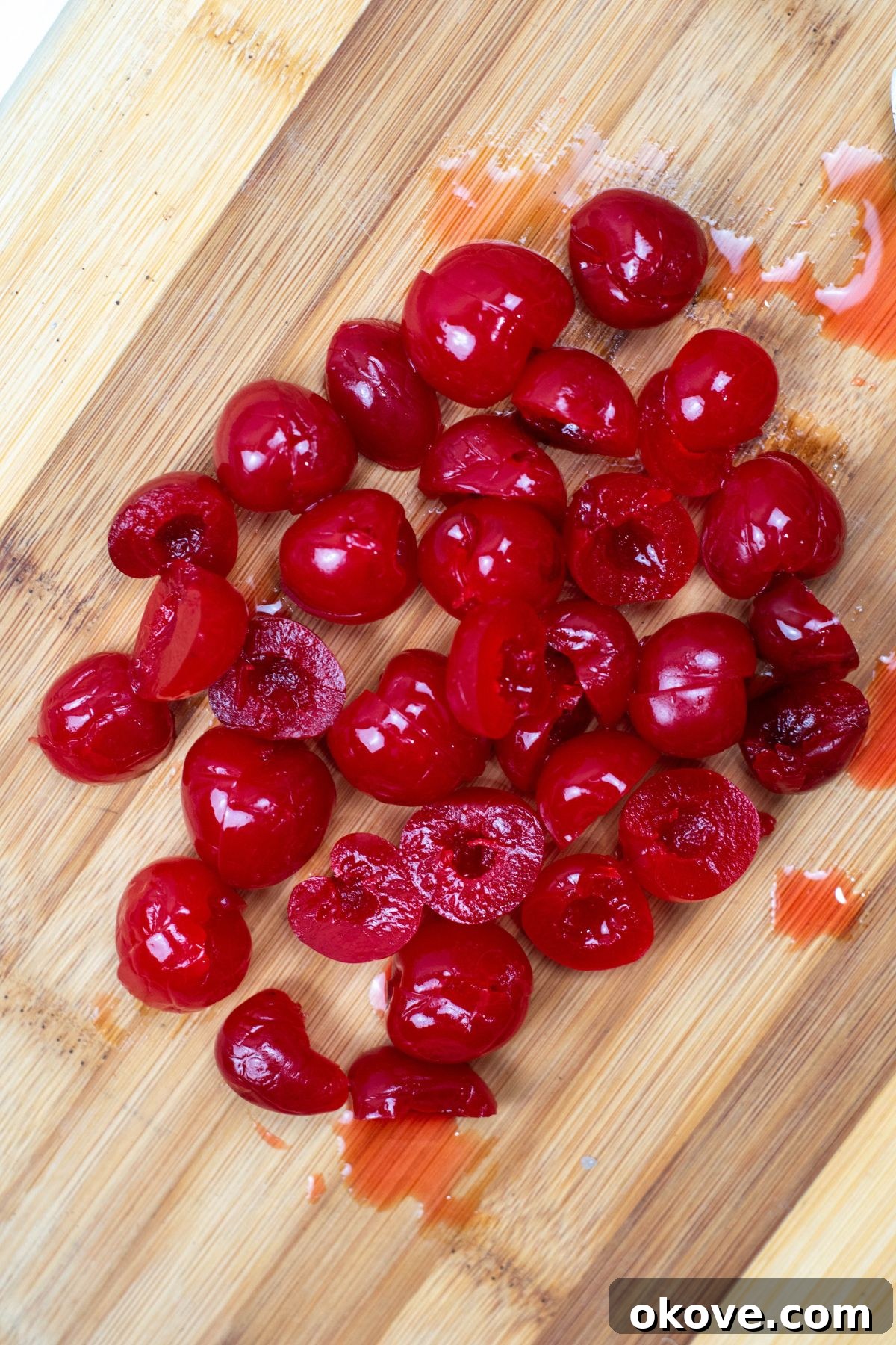 Maraschino cherries on a cutting board, being carefully sliced in half.