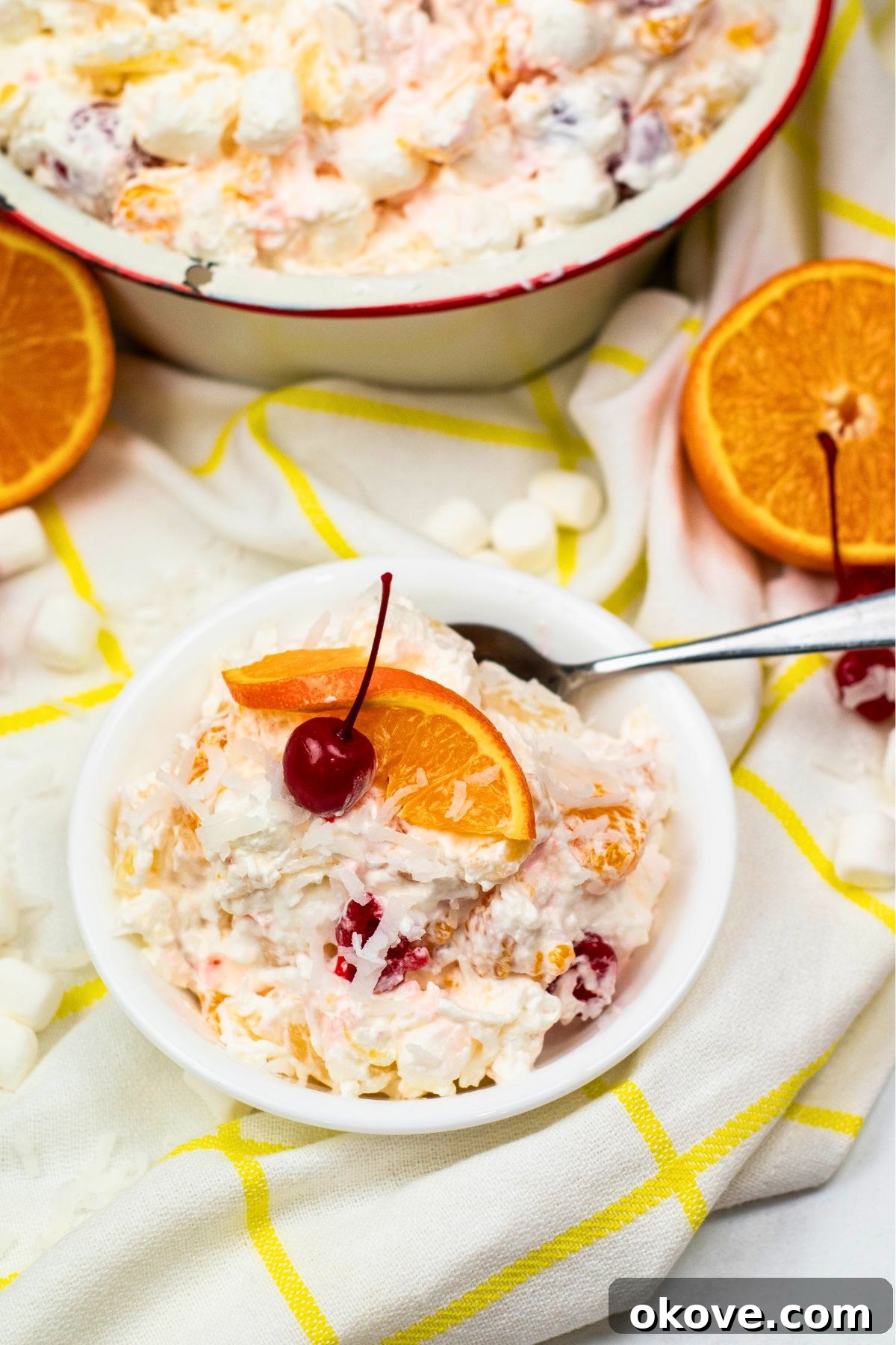 Small white bowl featuring a serving of Ambrosia fruit salad, with a spoon resting beside it, ready to be enjoyed.