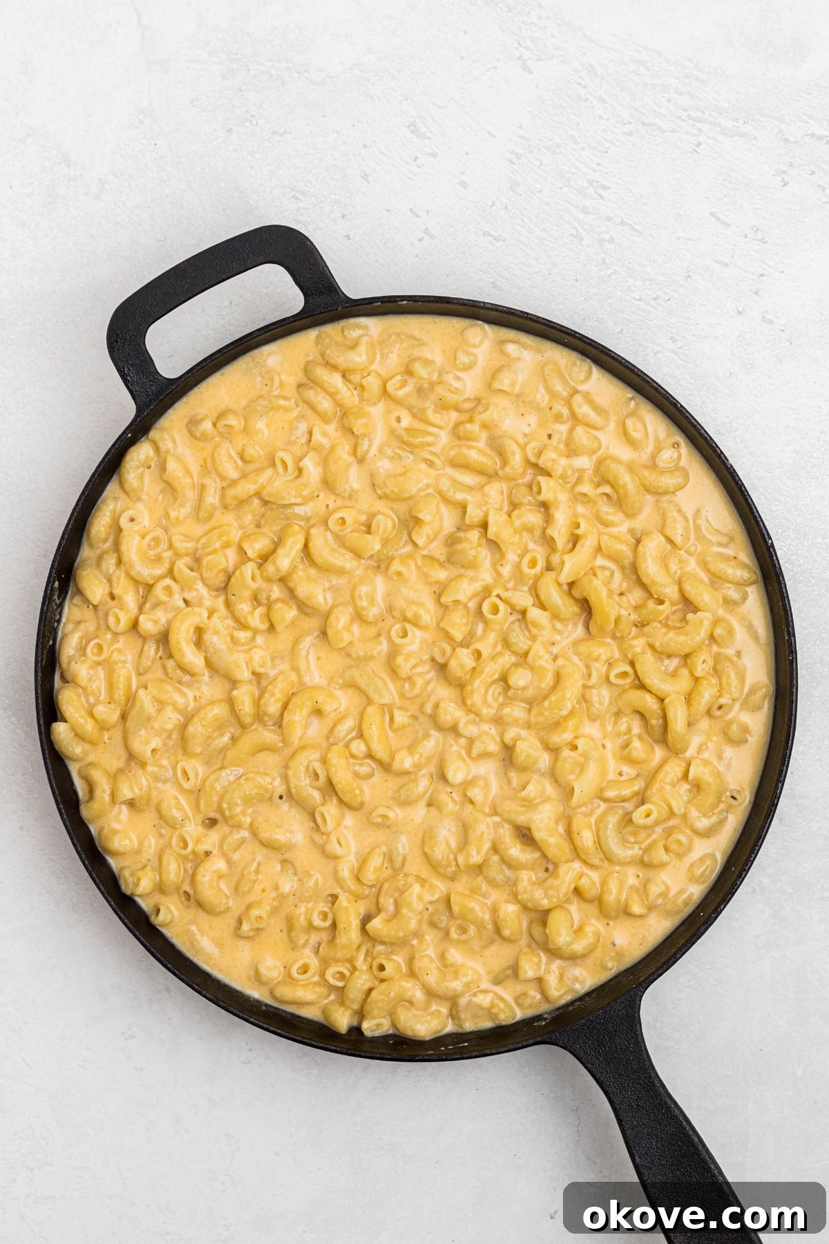 Ultimate Smoked Macaroni and Cheese Bake 7 Melted cheese mixture combined with pasta, in a cast iron skillet, on a white marble table.
