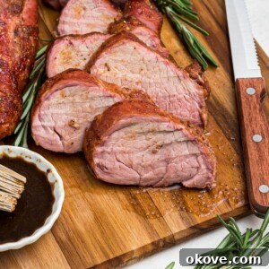 Smoky Pork Tenderloin Perfection 11 Juicy tenderloin cut into slices on a cutting board with a knife and fork, and fresh rosemary.