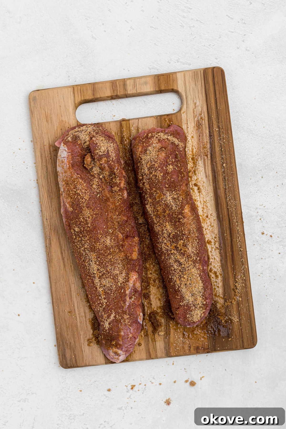 Smoky Pork Tenderloin Perfection 6 Uncooked, seasoned pork tenderloins resting on a wooden cutting board, ready to be placed in the smoker. The rub forms a beautiful crust.