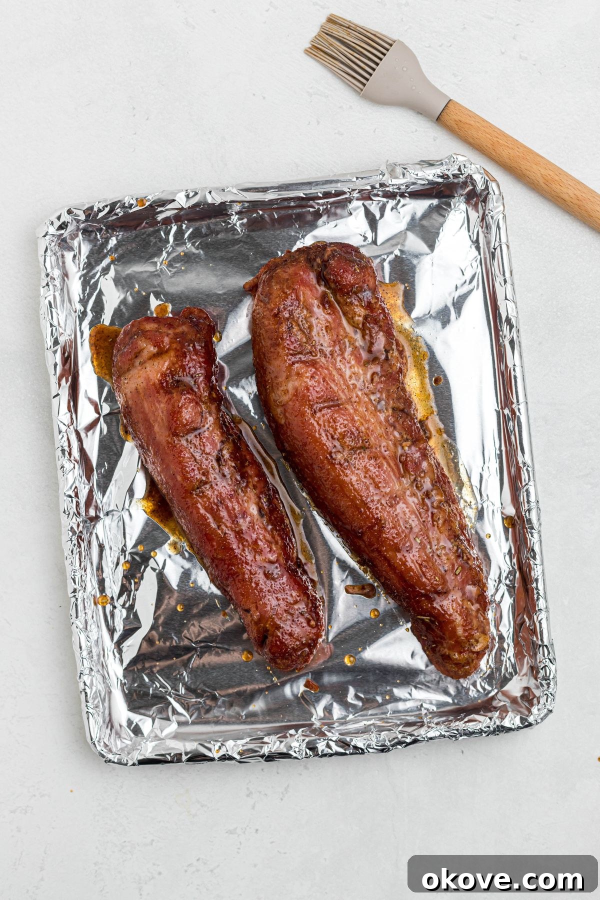 Smoky Pork Tenderloin Perfection 8 Juicy smoked tenderloins on a foil-covered baking sheet after being generously brushed with honey glaze, ready for a quick broil to caramelize the glaze.