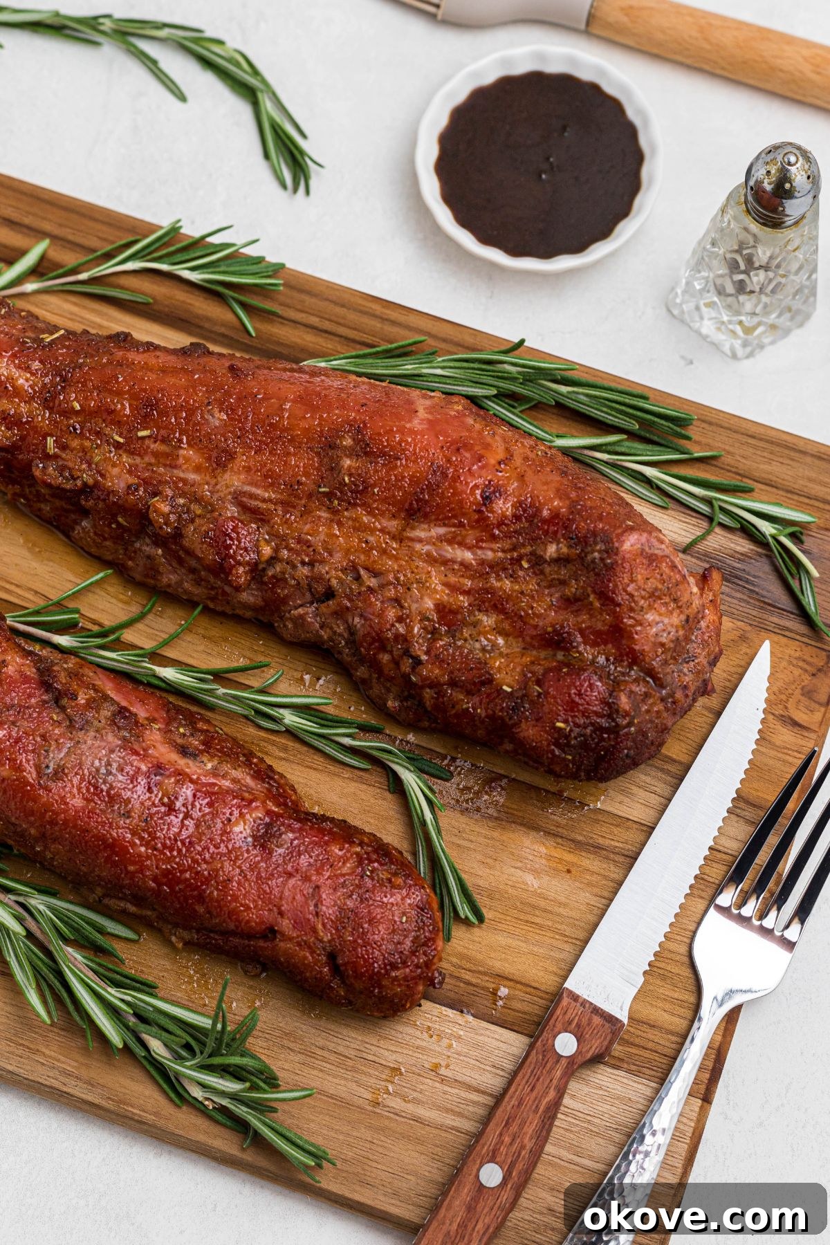 Smoky Pork Tenderloin Perfection 10 Smoked tenderloins on a wooden cutting board, after having a glossy glaze cooked on top, before being cut. The tenderloin is perfectly browned and ready for resting.