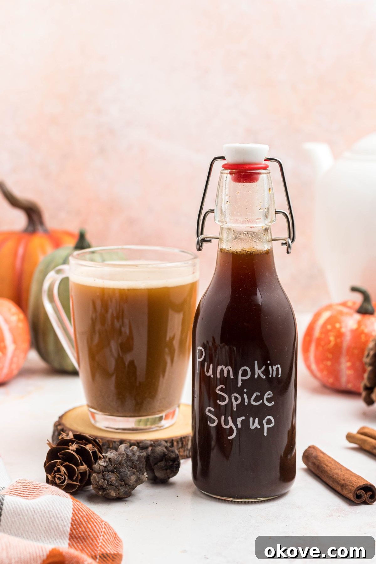 Golden Autumn Elixir 8 Bottle of pumpkin spice syrup on a small wooden coaster next to a cup of coffee, on a marble table.
