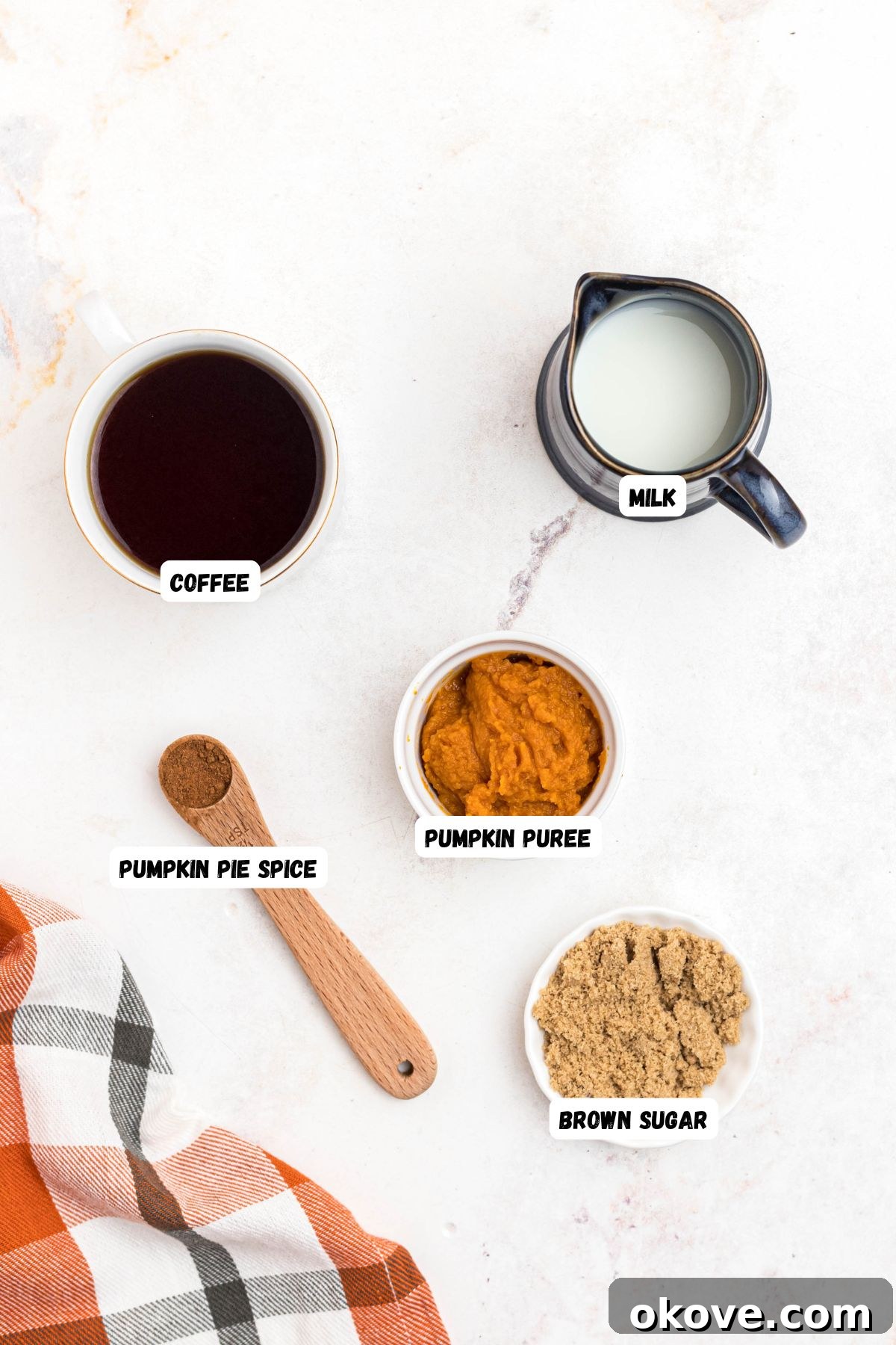 Cozy Pumpkin Spice Brew 3 Ingredients for homemade pumpkin spice coffee, including hot brewed coffee, pumpkin puree, maple syrup, pumpkin pie spice, and milk, measured into small bowls on a marble surface.