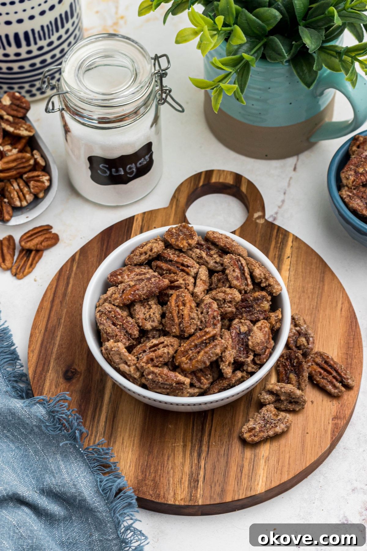 Sweet Pecan Crunch 2 Sugar coated pecans in a white bowl with a small jar of sugar behind the bowl. A perfect serving of homemade candied pecans.