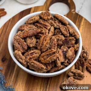 Sweet Pecan Crunch 11 Sugar coated pecans in a white bowl with a small jar of sugar behind the bowl. Delicious candied pecans in a serving bowl.