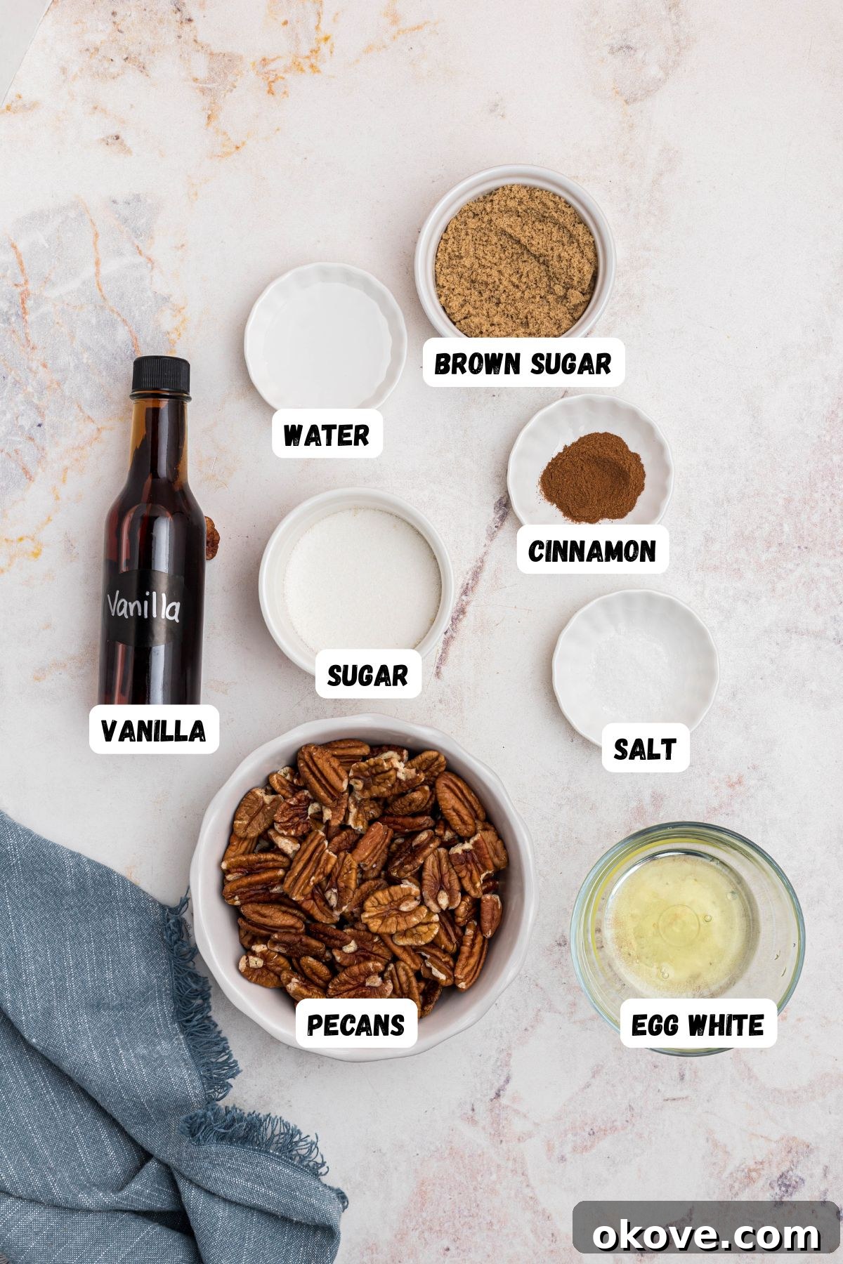 Sweet Pecan Crunch 3 Ingredients needed to make candied pecans measured into small bowls and labeled on a marble table. Clearly laid out ingredients for making candied pecans.