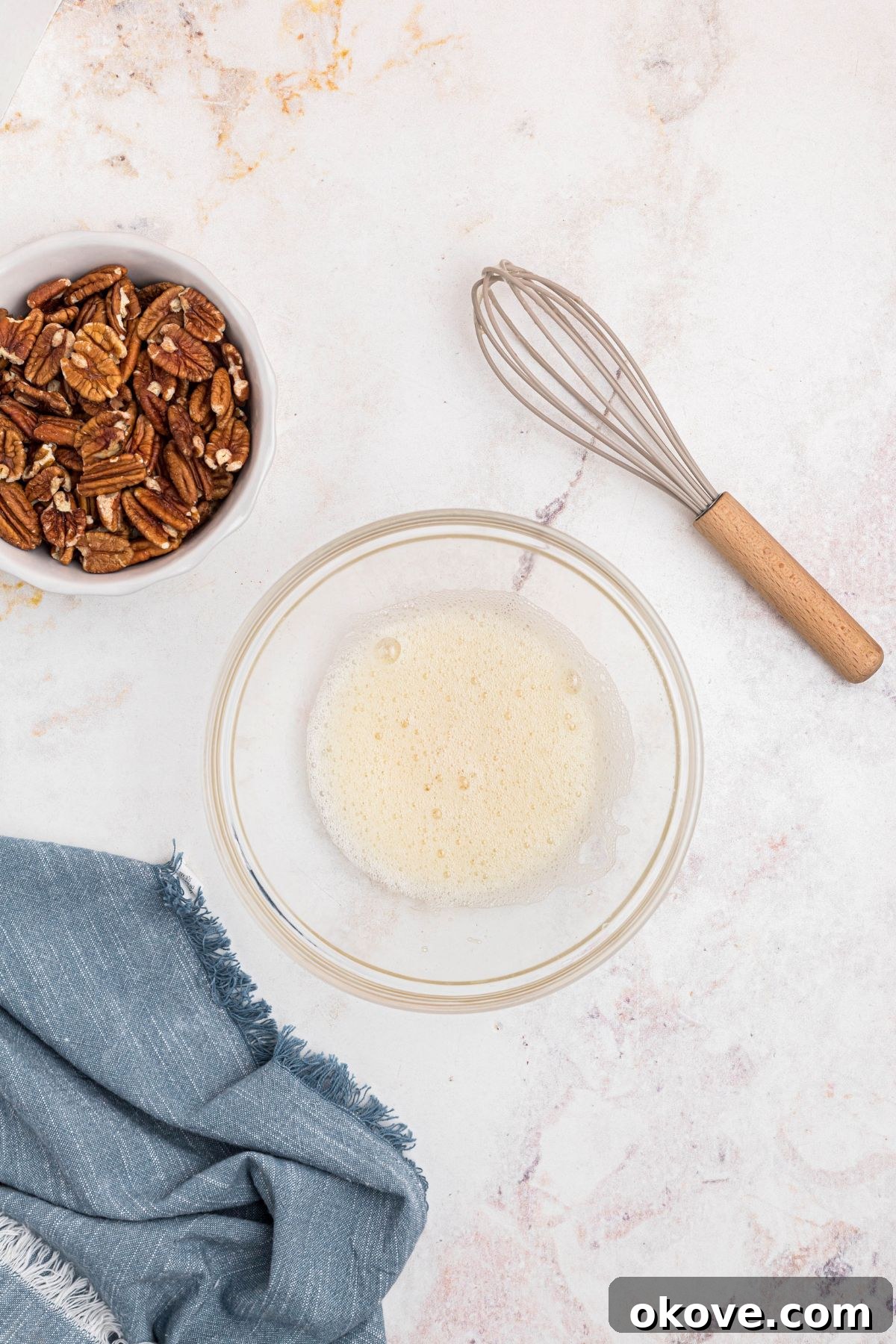 Sweet Pecan Crunch 4 Egg white whisked with water and vanilla in a clear glass bowl, frothy texture.