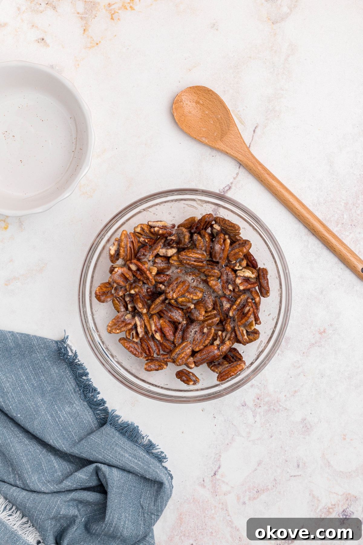 Sweet Pecan Crunch 5 Pecans being tossed together with whisked egg white mixture in a clear glass bowl.
