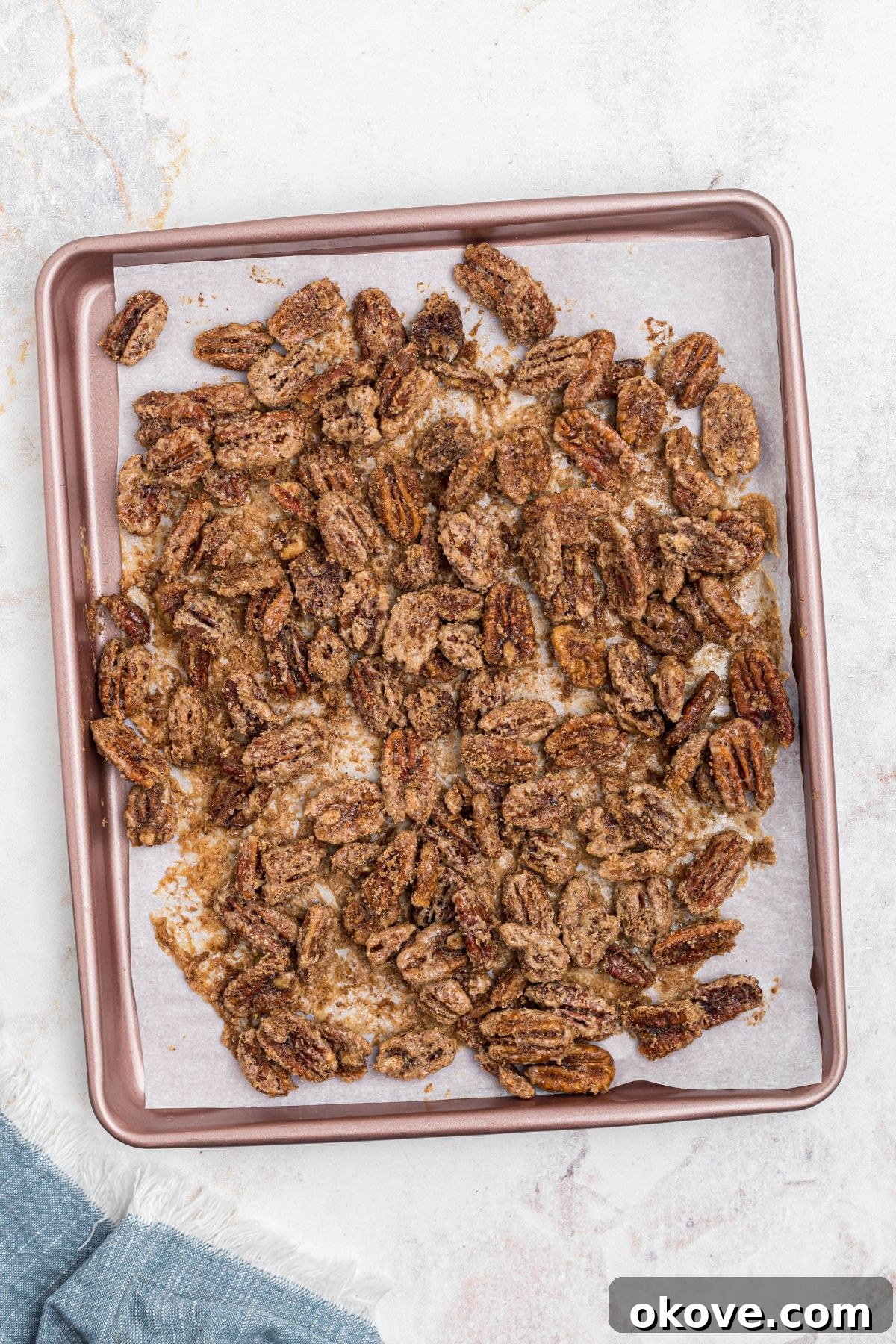 Sweet Pecan Crunch 9 Pecans on baking sheet lined with parchment paper, coated with sugar, after baking, golden brown and separated.