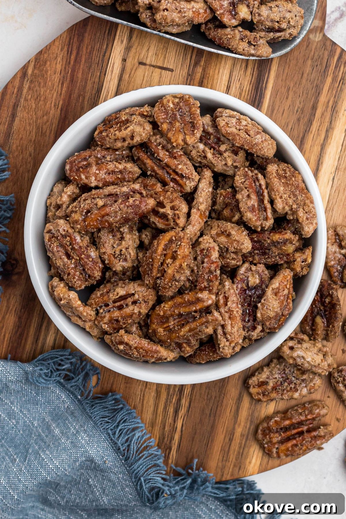 Sweet Pecan Crunch 10 Candied pecans in a small white bowl, with a blue linen and scattered pecans nearby. Beautifully presented candied pecans.