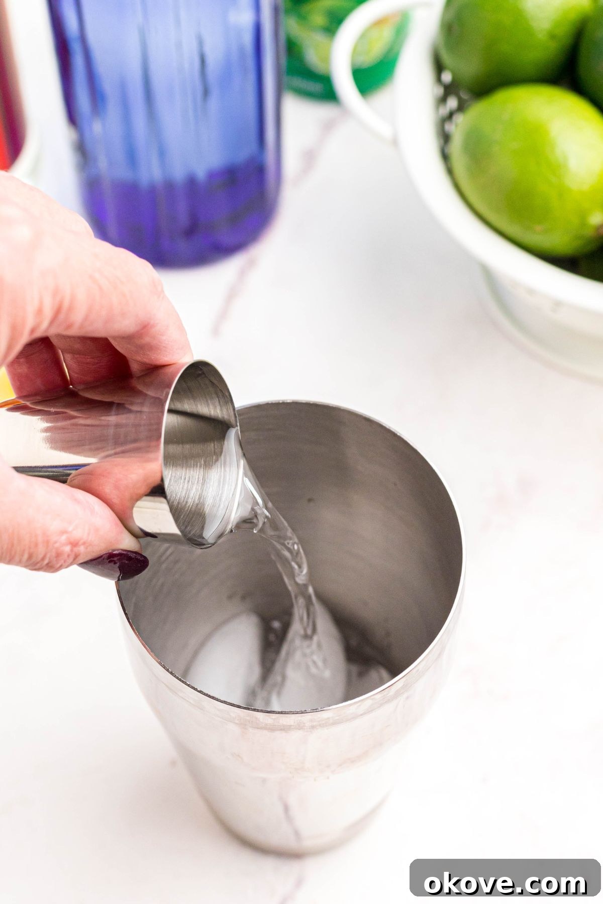 The initial step in crafting a Kamikaze shot, illustrating the precise moment alcohol is poured into a cocktail shaker brimming with ice, setting the stage for perfect chilling and mixing.
