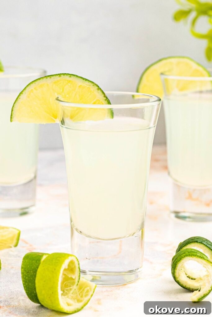 A vibrant display of freshly prepared Kamikaze shots, artfully arranged on a sleek marble table, each glass impeccably garnished with a bright lime wedge, showcasing their readiness for a lively gathering.