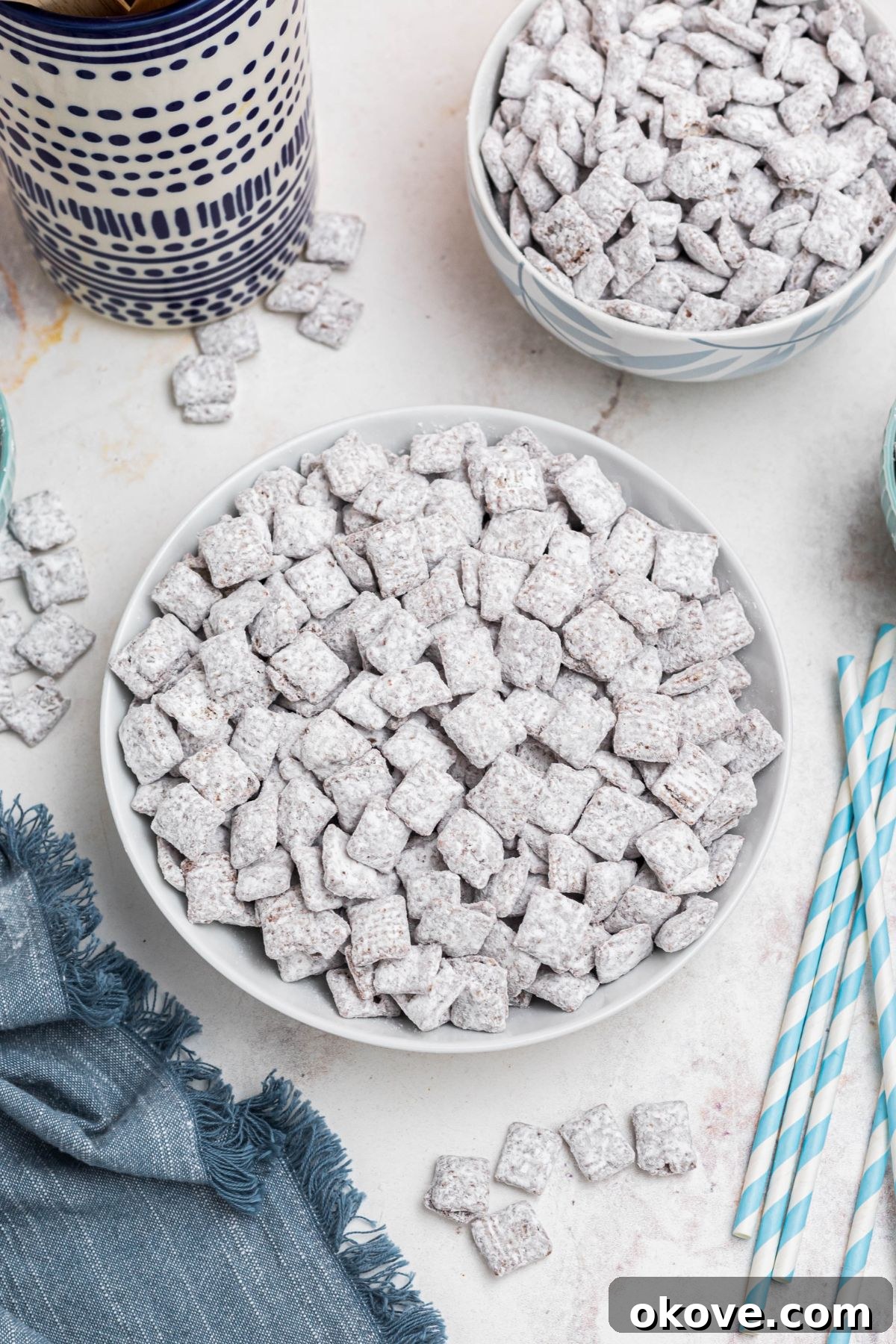 White bowl filled with powdered sugar coated cereal pieces, with blue linen and straws on the table. 