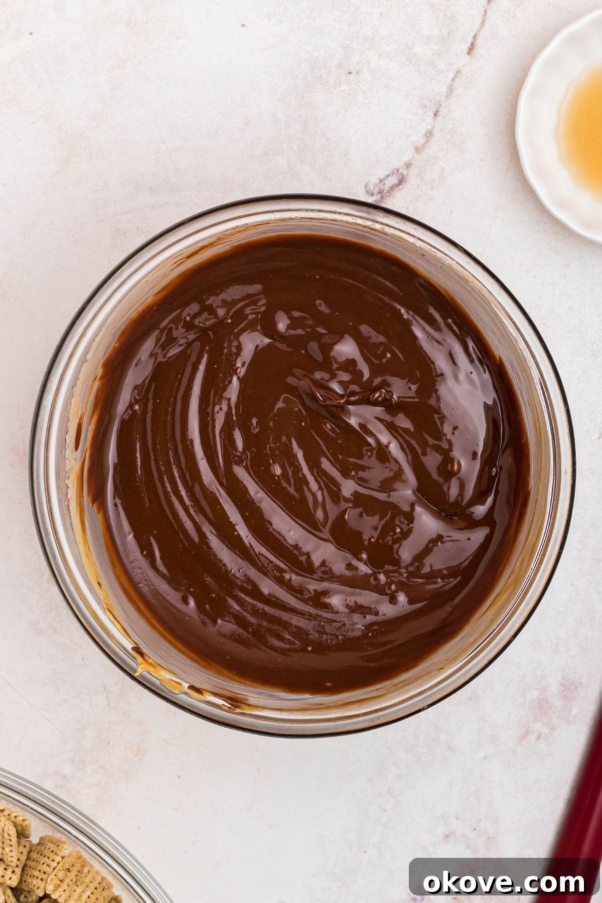Melted chocolate and peanut butter, and butter, mixed together in a clear glass bowl. 