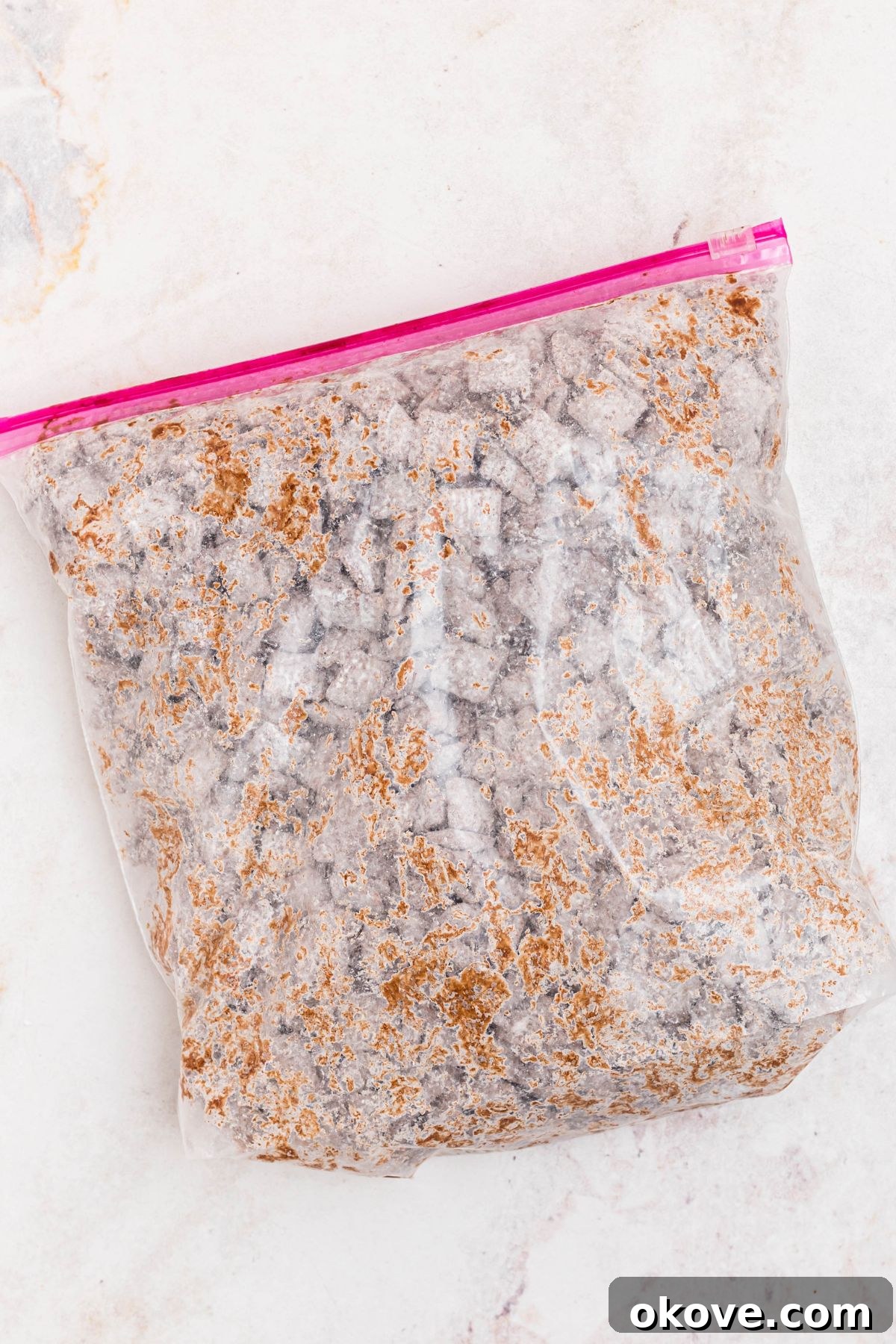 Powdered sugar being mixed in with chocolate coated cereal in a large mixing bag. 