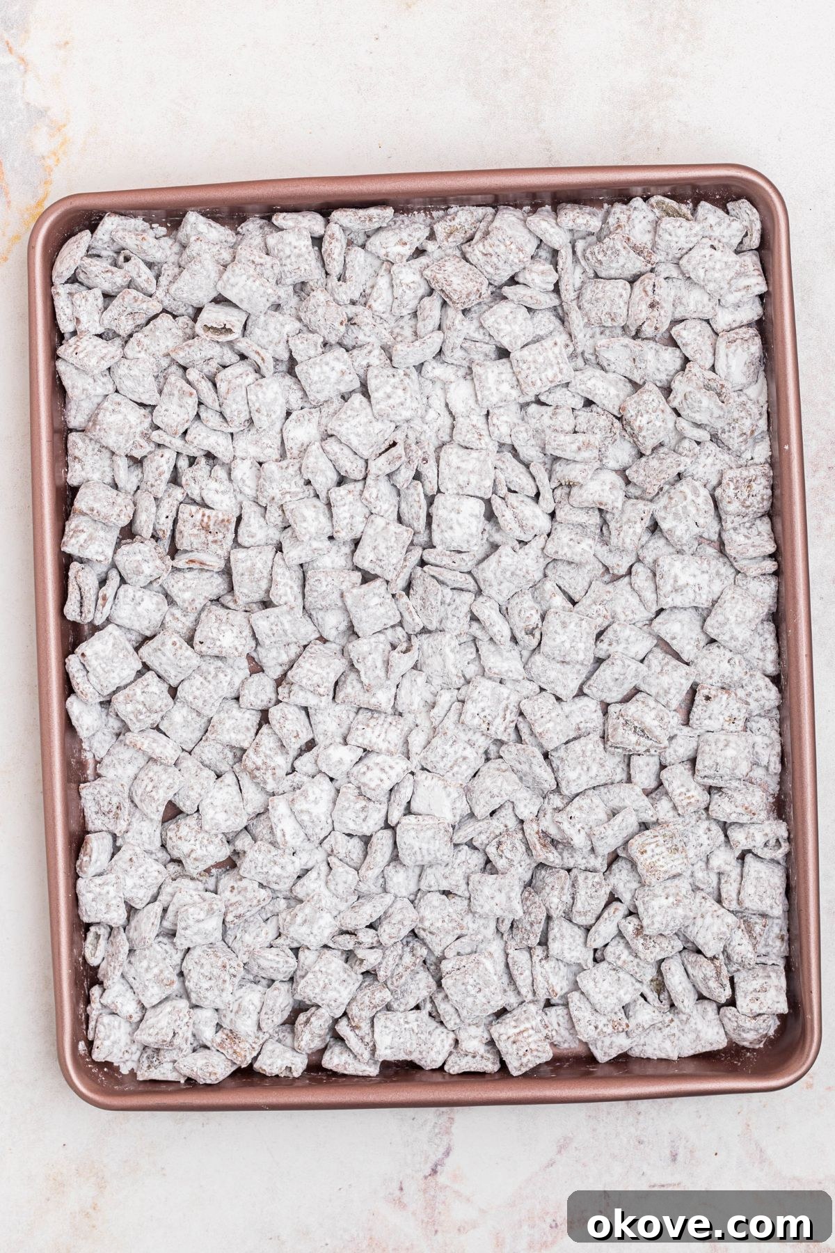 Coated Chex cereal spread out and cooling on a baking sheet. 