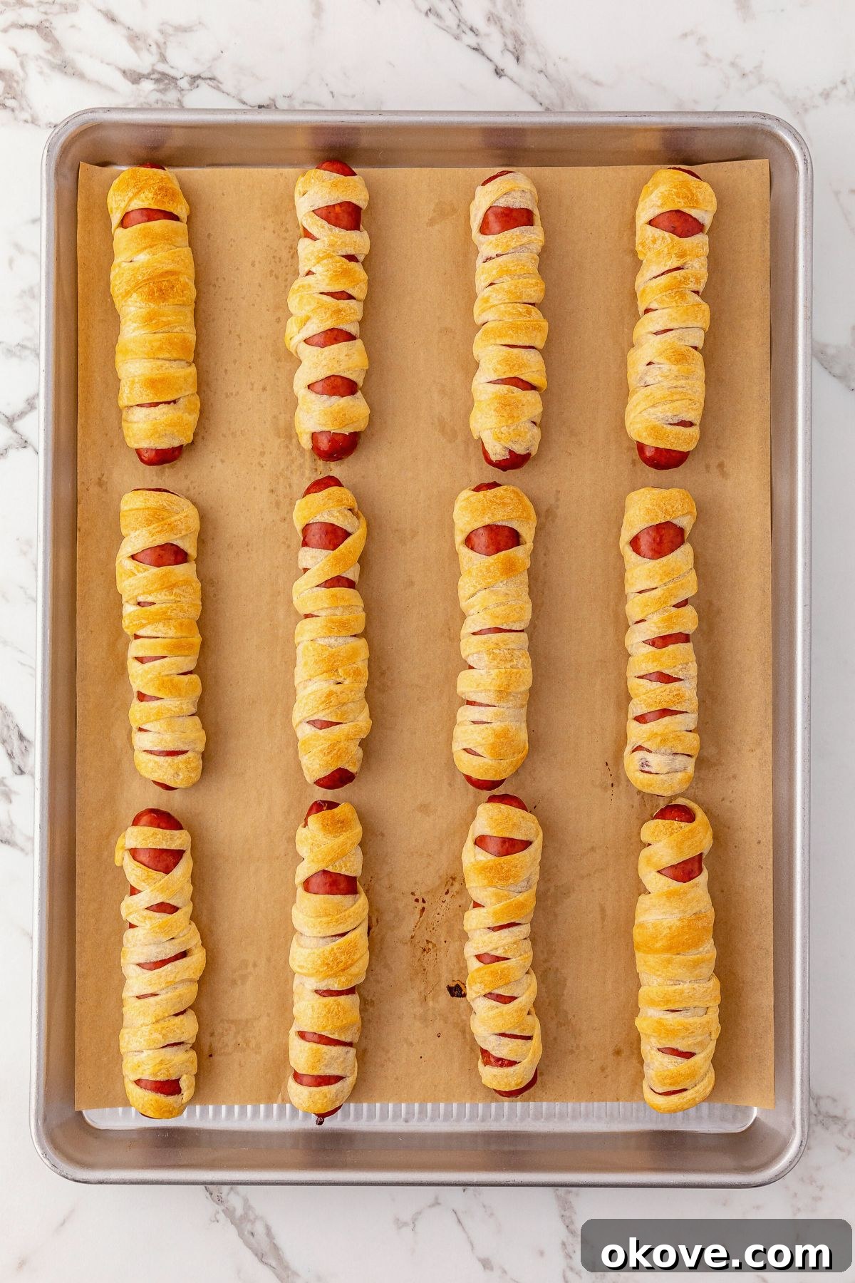Mummy Hot Dogs 6 Mummy hot dogs, perfectly wrapped in dough strips, baked to a golden brown perfection on a baking sheet, ready for final touches.