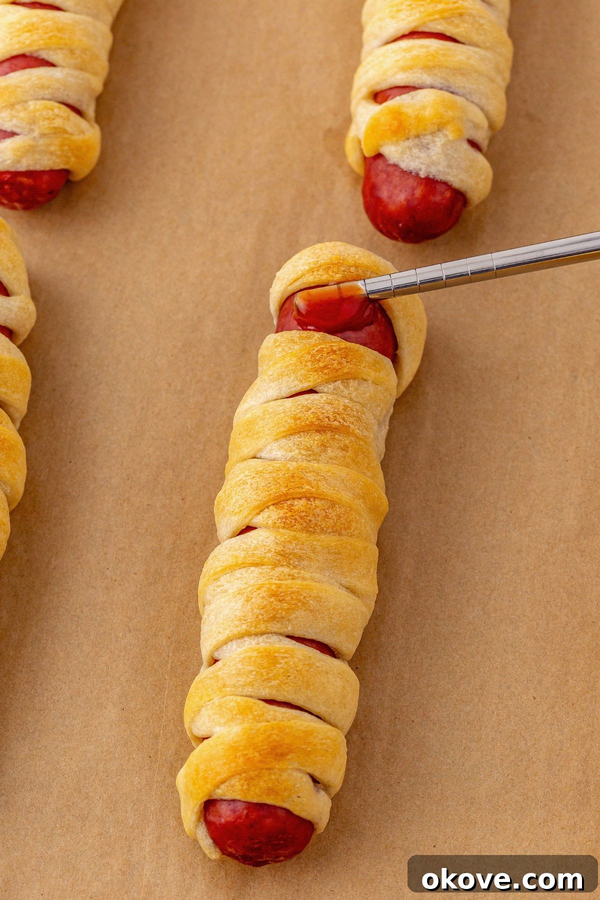 Mummy Hot Dogs 7 A small dab of ketchup being carefully applied to a baked mummy hot dog, creating the perfect adhesive spot for attaching candy eyes.