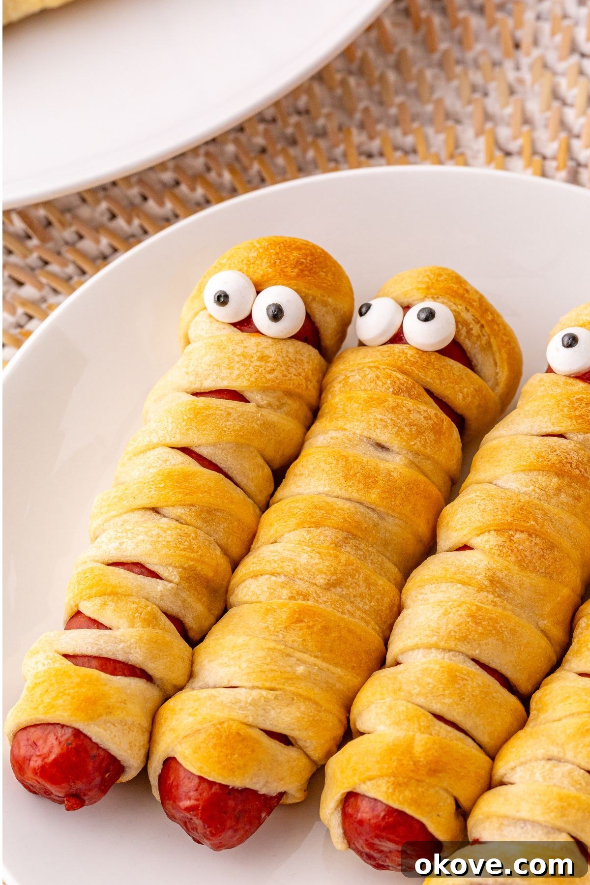 Mummy Hot Dogs 8 A festive display of Mummy hot dogs on a crisp white plate, each adorned with playful candy eyes, ready to be enjoyed as a spooky treat.