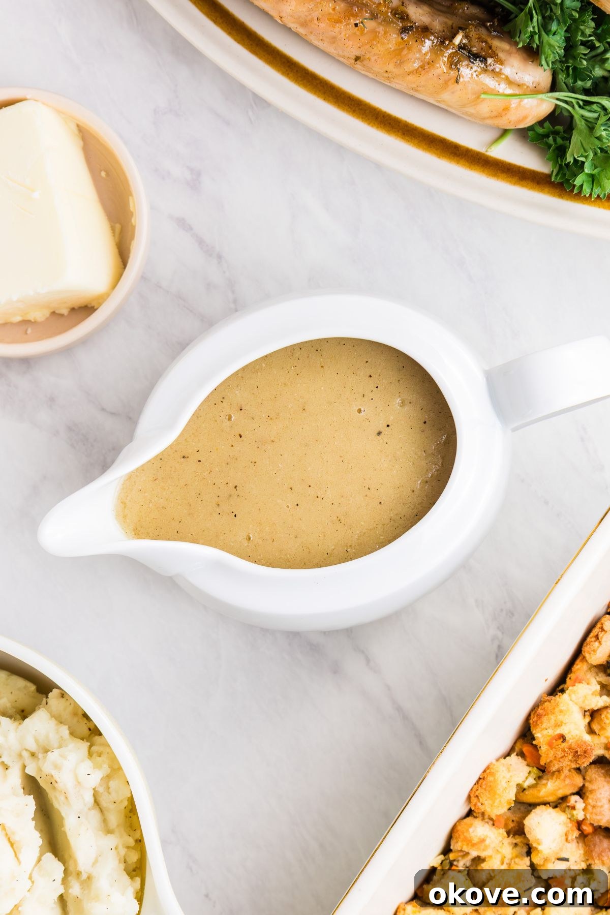 From Pan Drippings to Perfection 2 White gravy boat filled with creamy gravy, served with other holiday dishes, on a white marble table.