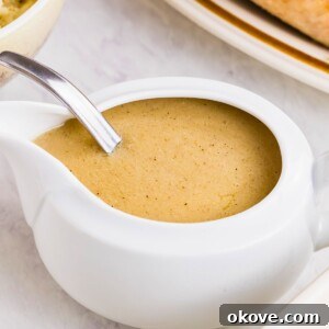White gravy boat filled with creamy gravy, served with other holiday dishes, on a white marble table.