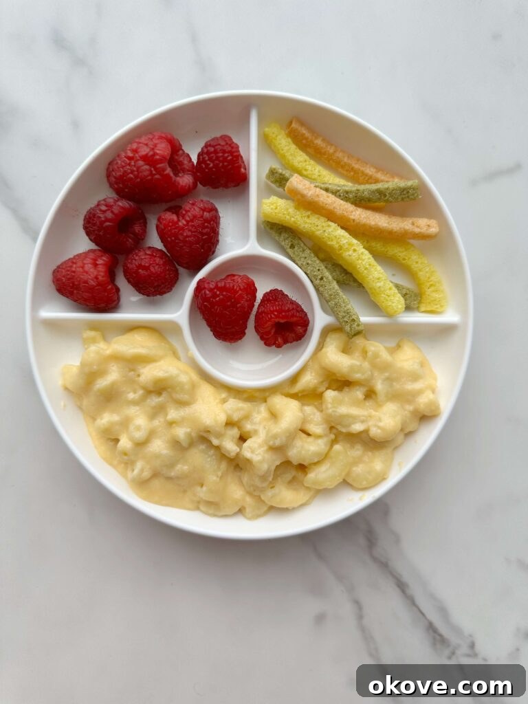 Irresistible Cauliflower Mac and Cheese 2 Cauliflower mac n cheese in a divided plate with raspberries and vegetable straws, presented attractively for a toddler meal.